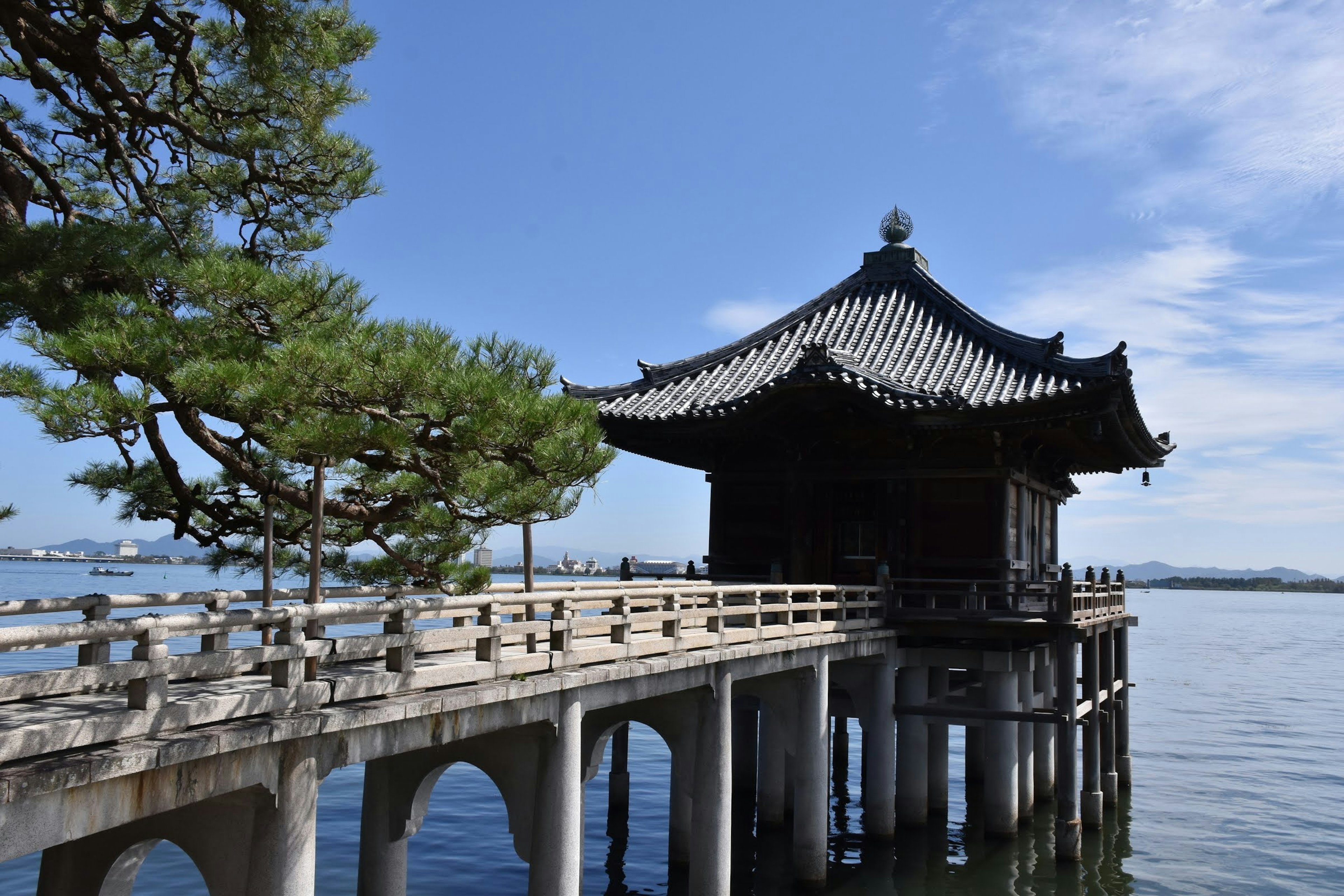 Traditional Chinese-style building standing over a serene lake with a wooden bridge