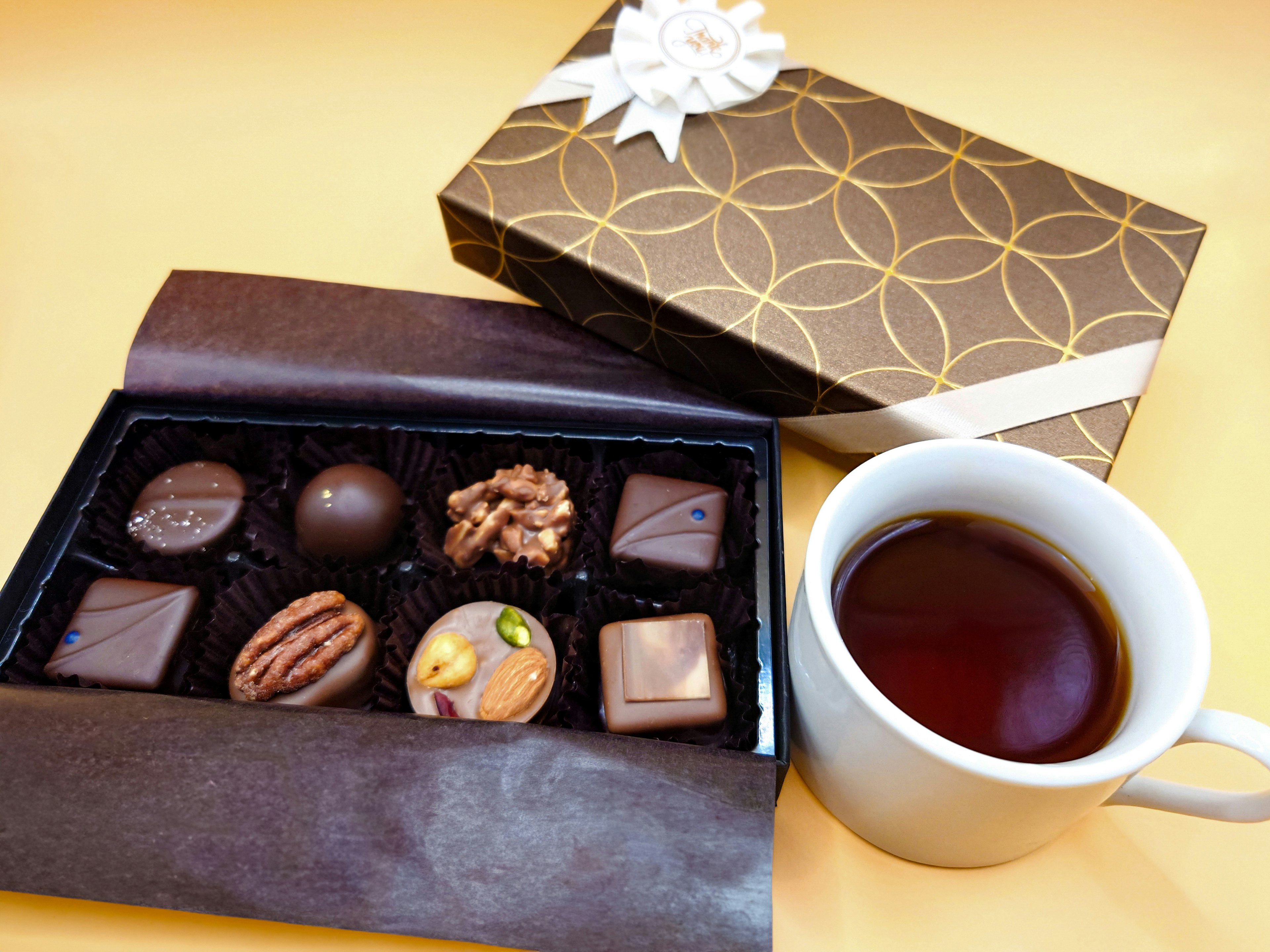 Una mesa hermosa con una caja de chocolates surtidos y una taza de café