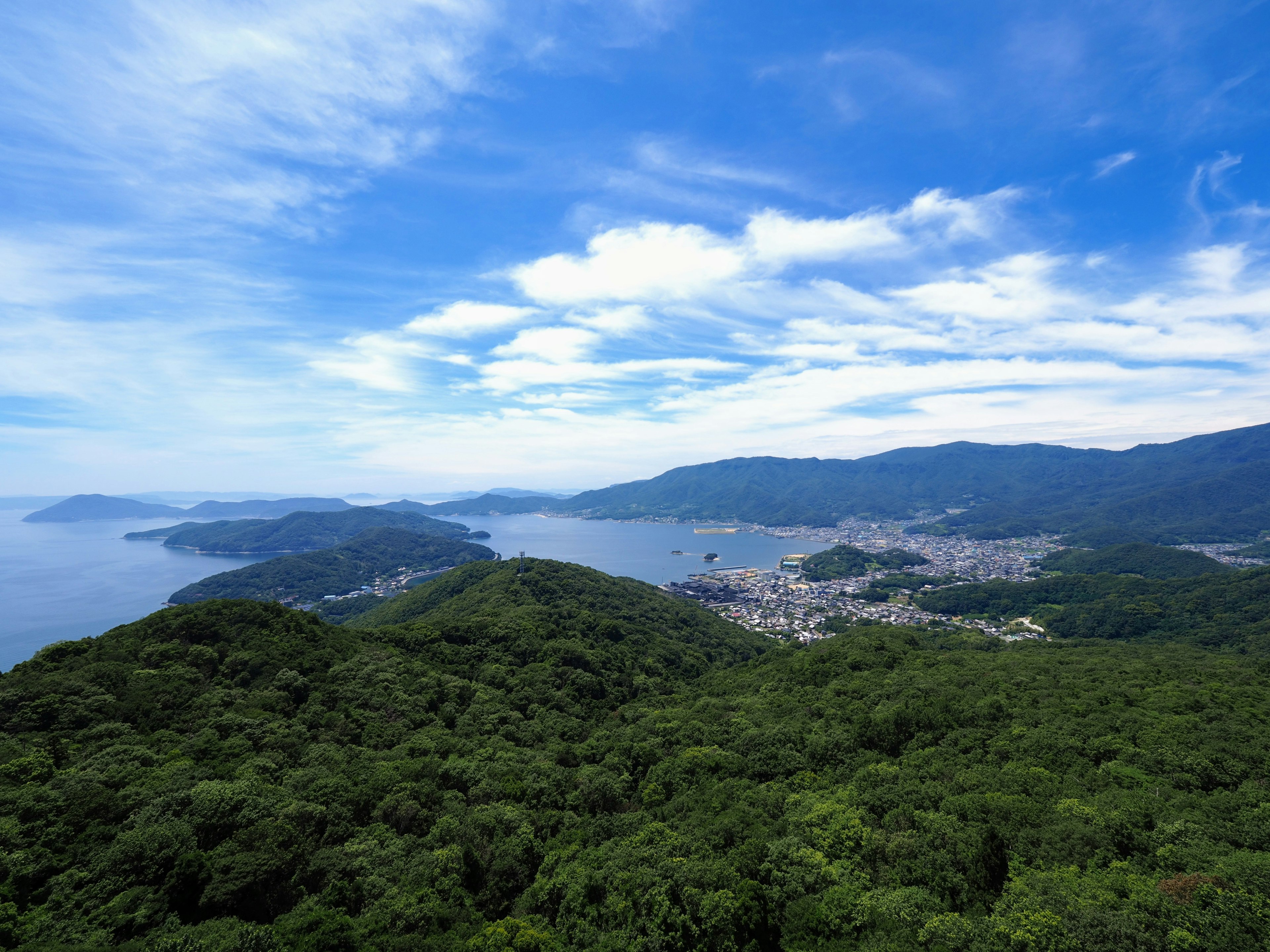 Lush green hills overlooking a bay under a blue sky with clouds