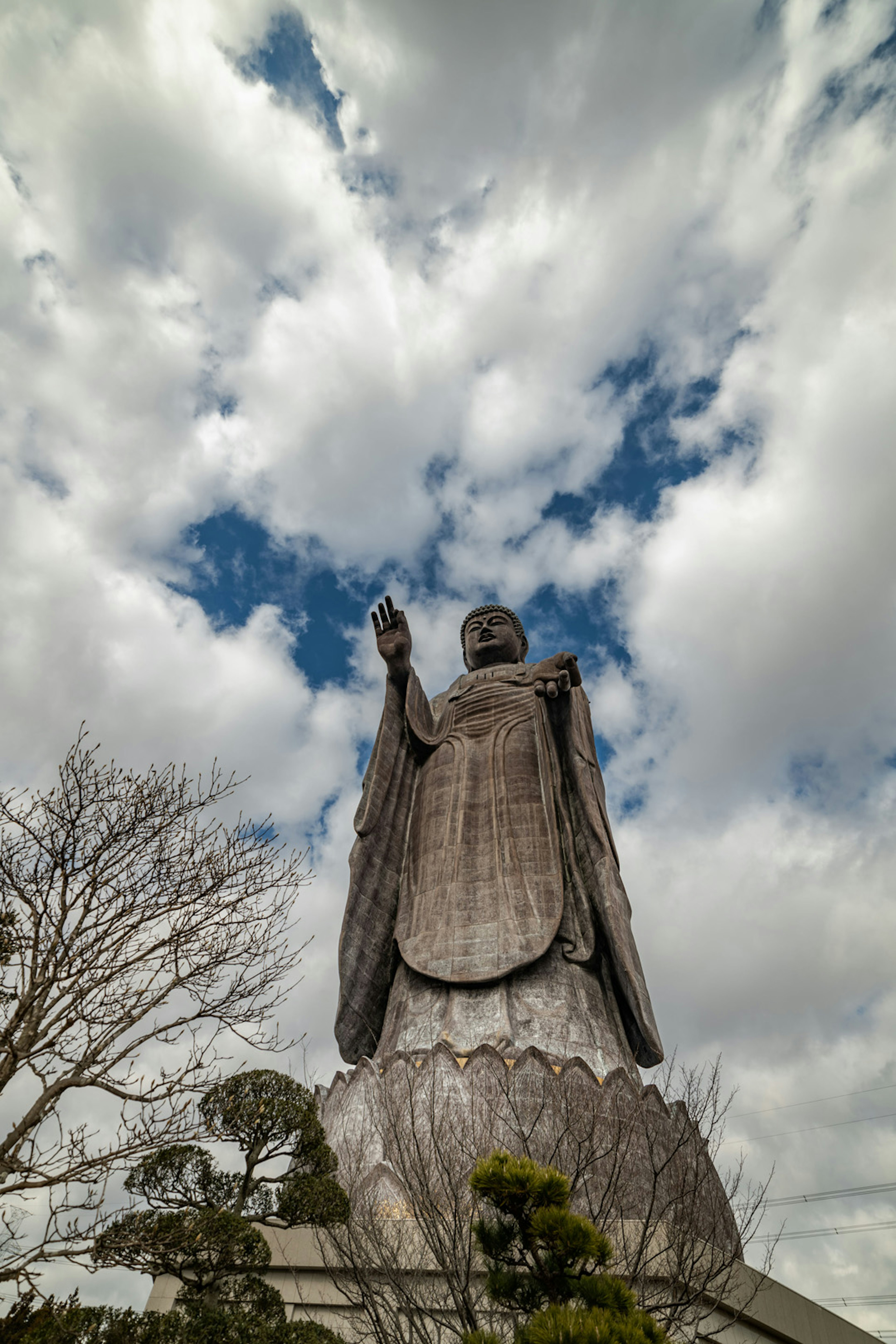 Large statue of a Buddha figure with raised hand against a cloudy sky