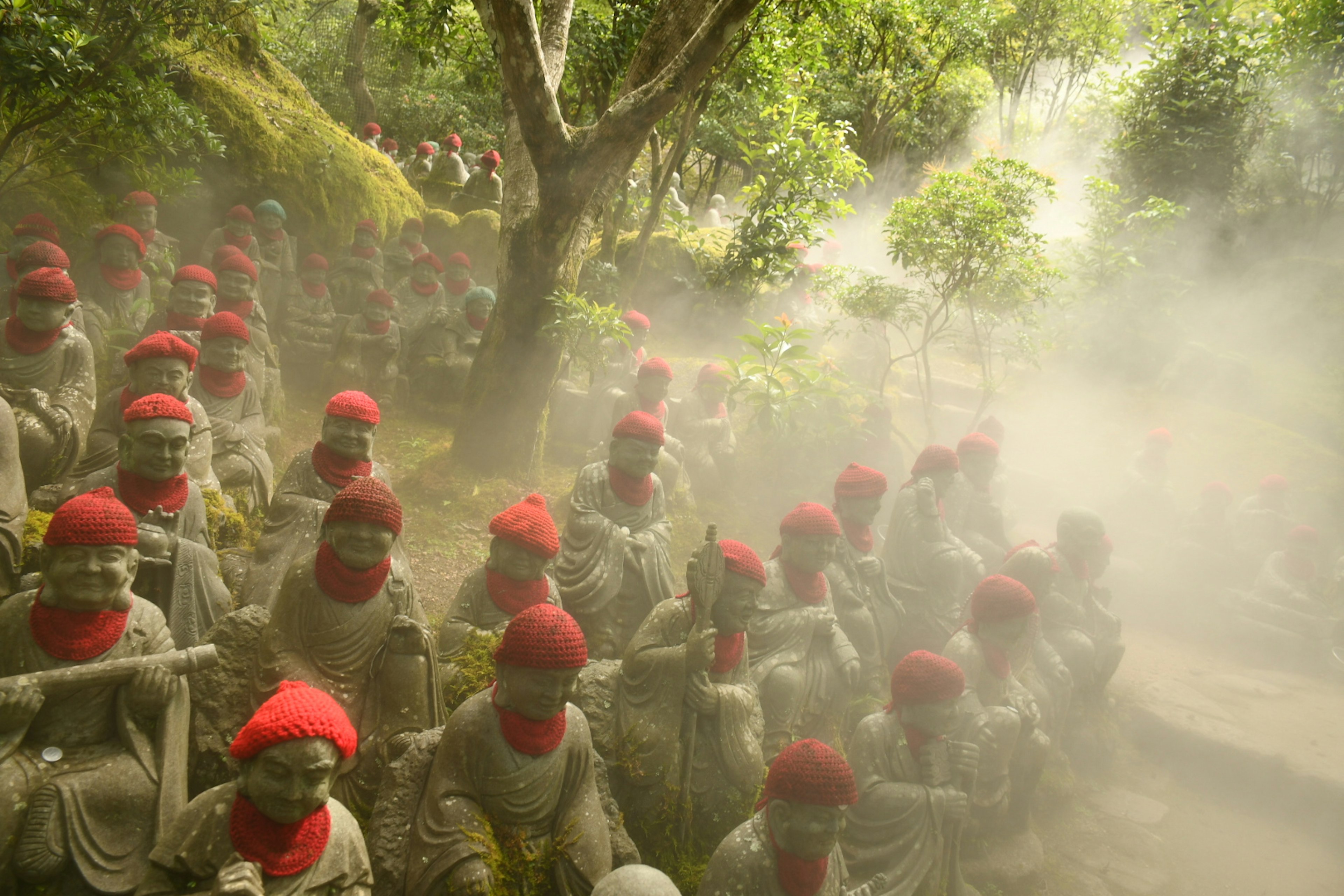 Estatuas de piedra con sombreros rojos dispuestas en un paisaje brumoso