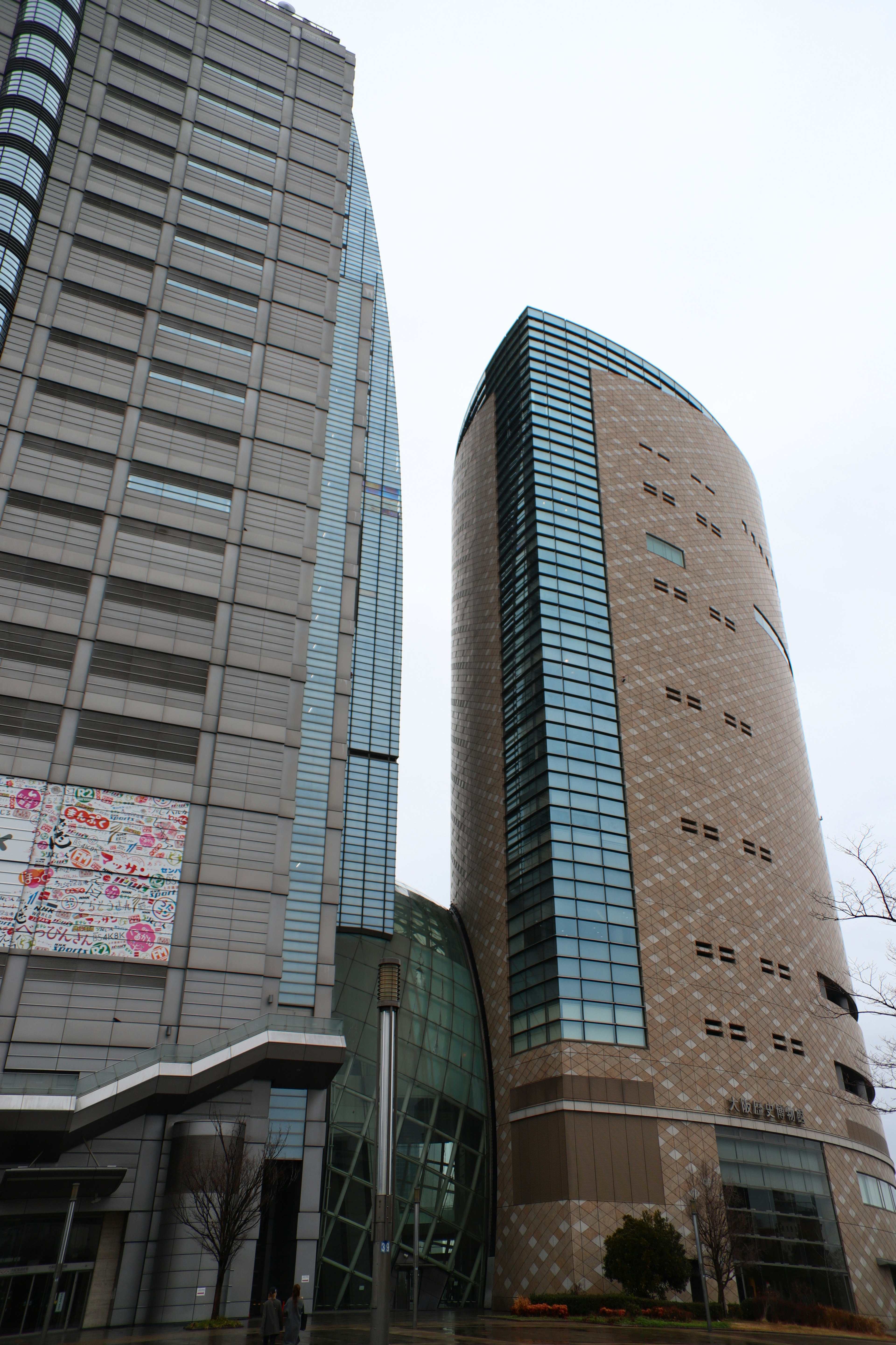 Two modern buildings standing side by side, left one has a linear gray facade, right one features a curved glass design