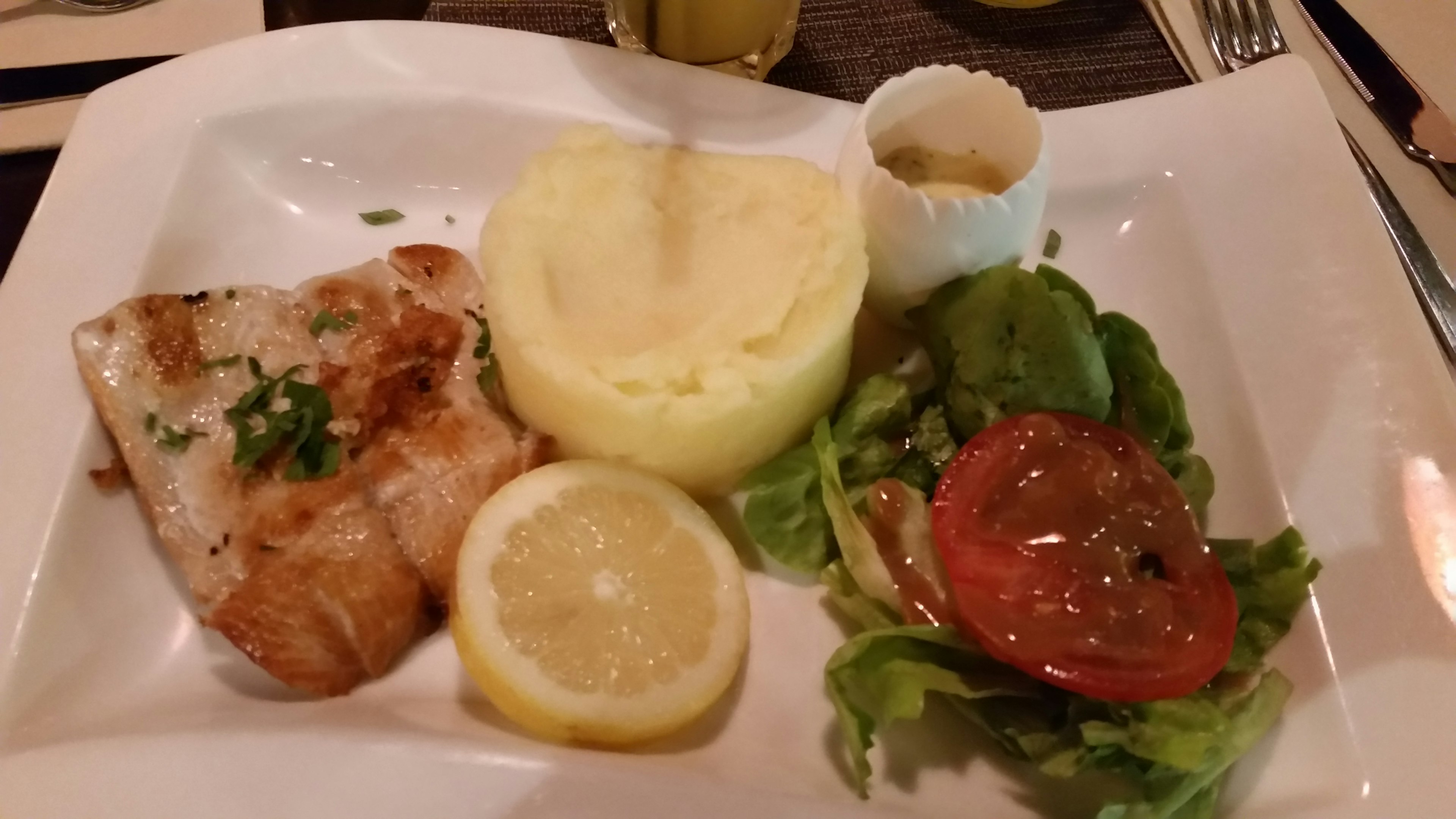 Grilled white fish served with mashed potatoes, salad, and lemon slices