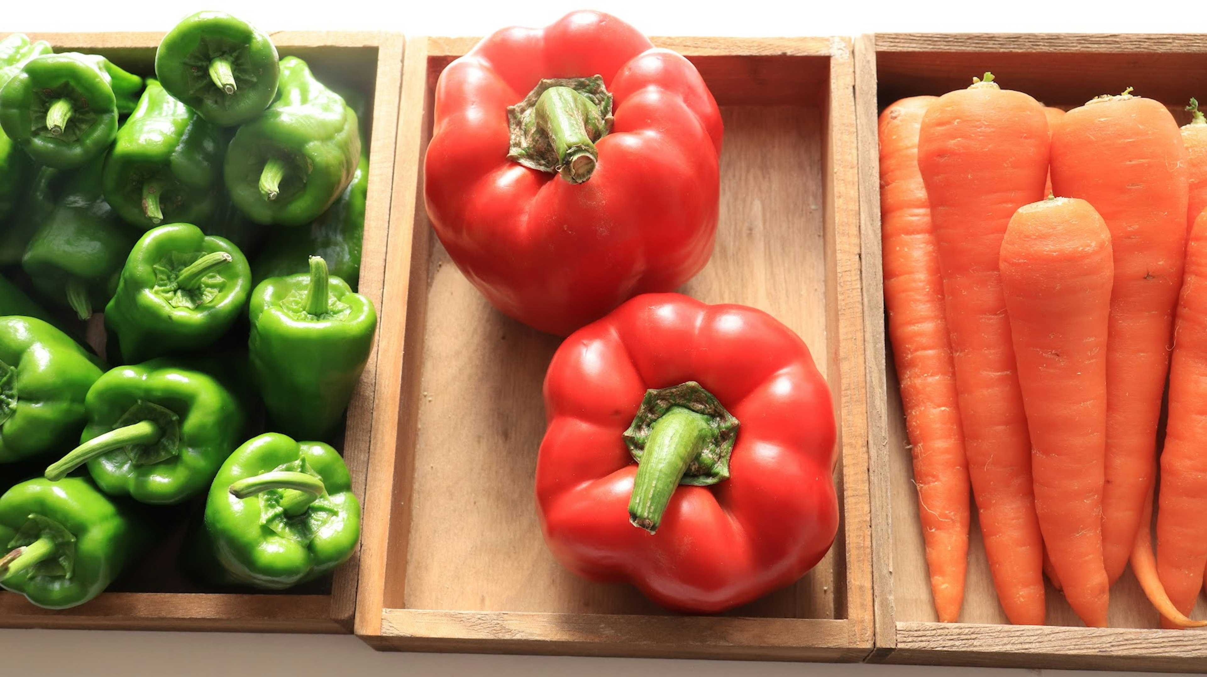 Green and red bell peppers along with orange carrots arranged in wooden boxes