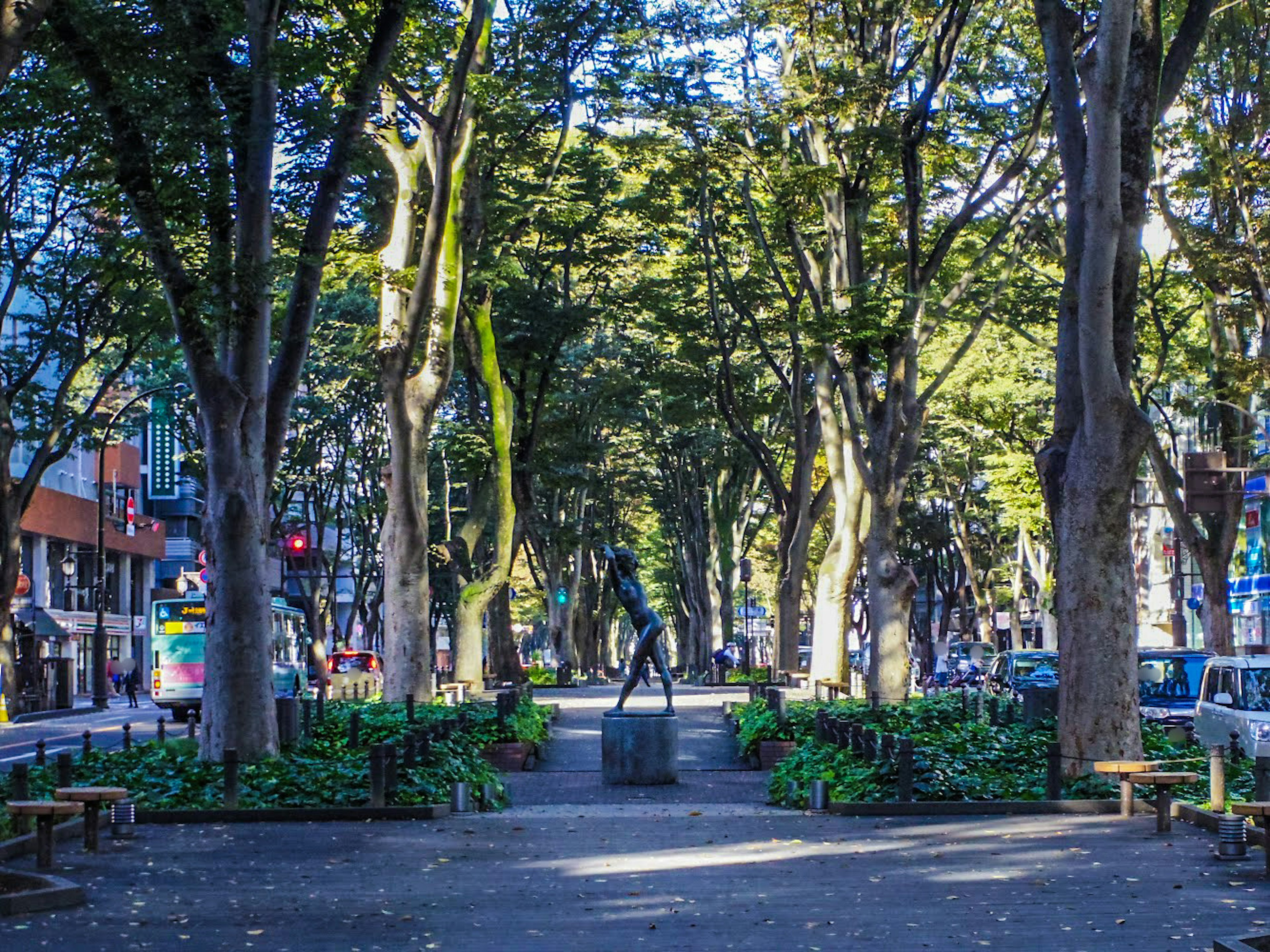 Camino del parque bordeado de árboles verdes y una estatua