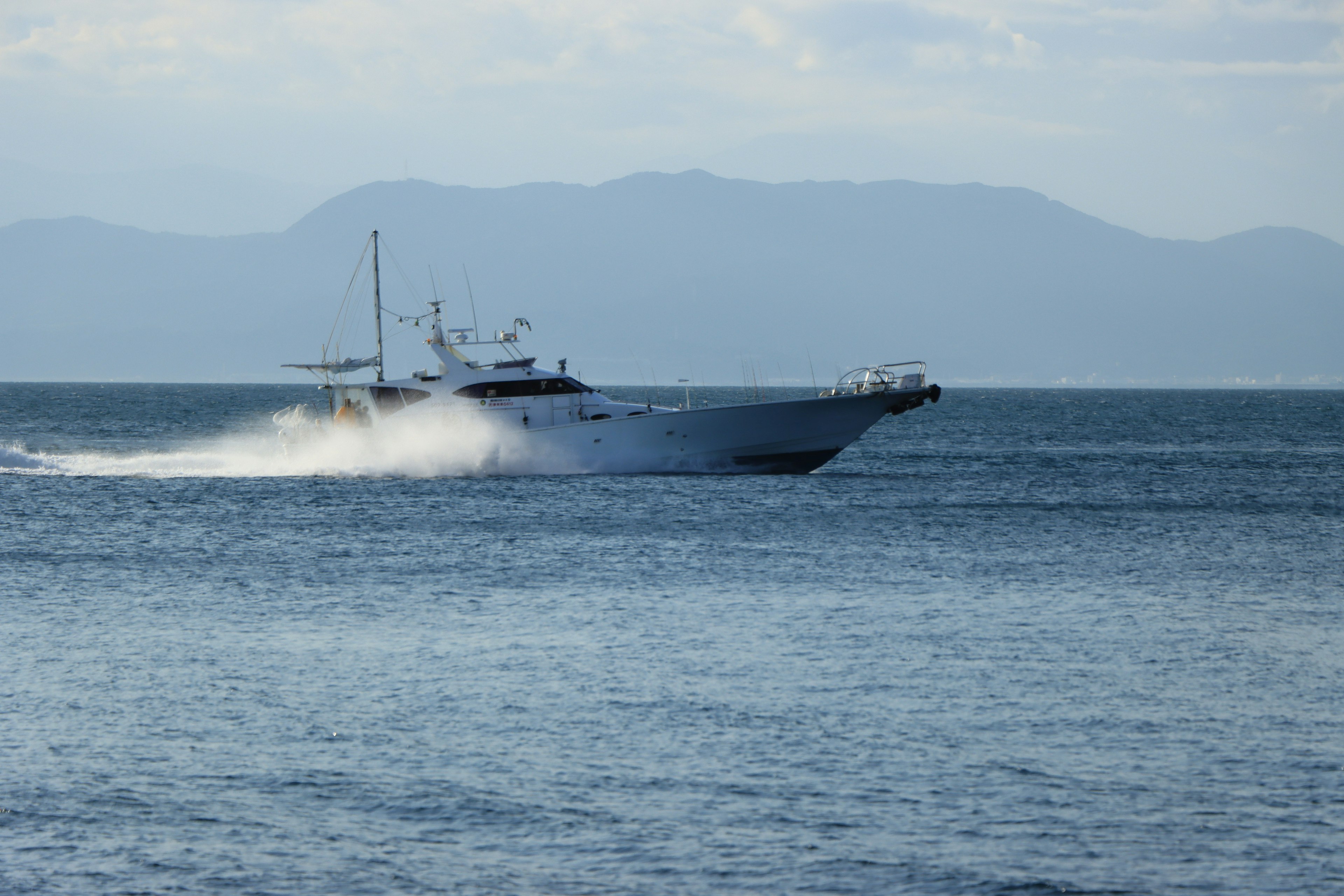 Weißes Boot gleitet über das Meer mit Bergen im Hintergrund