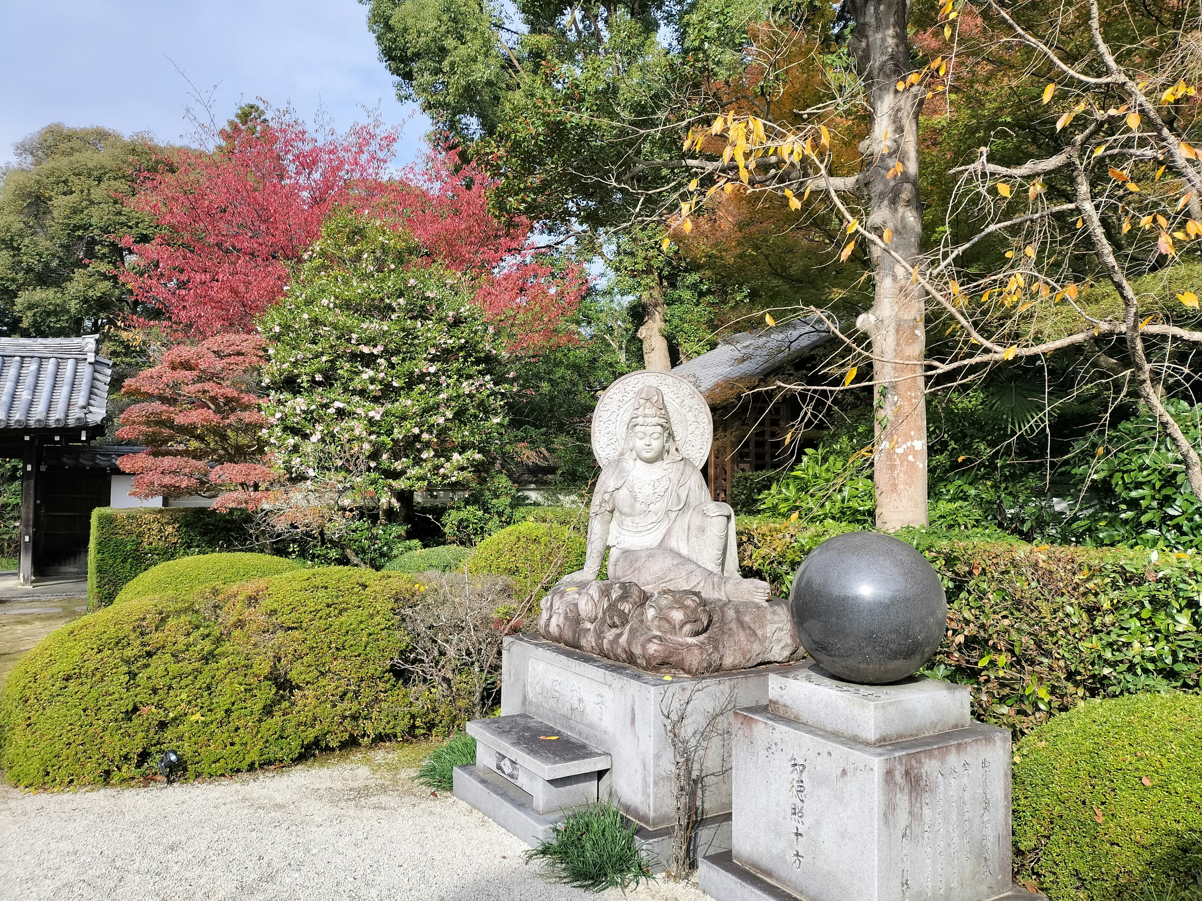 Stone statue in a serene garden with colorful trees