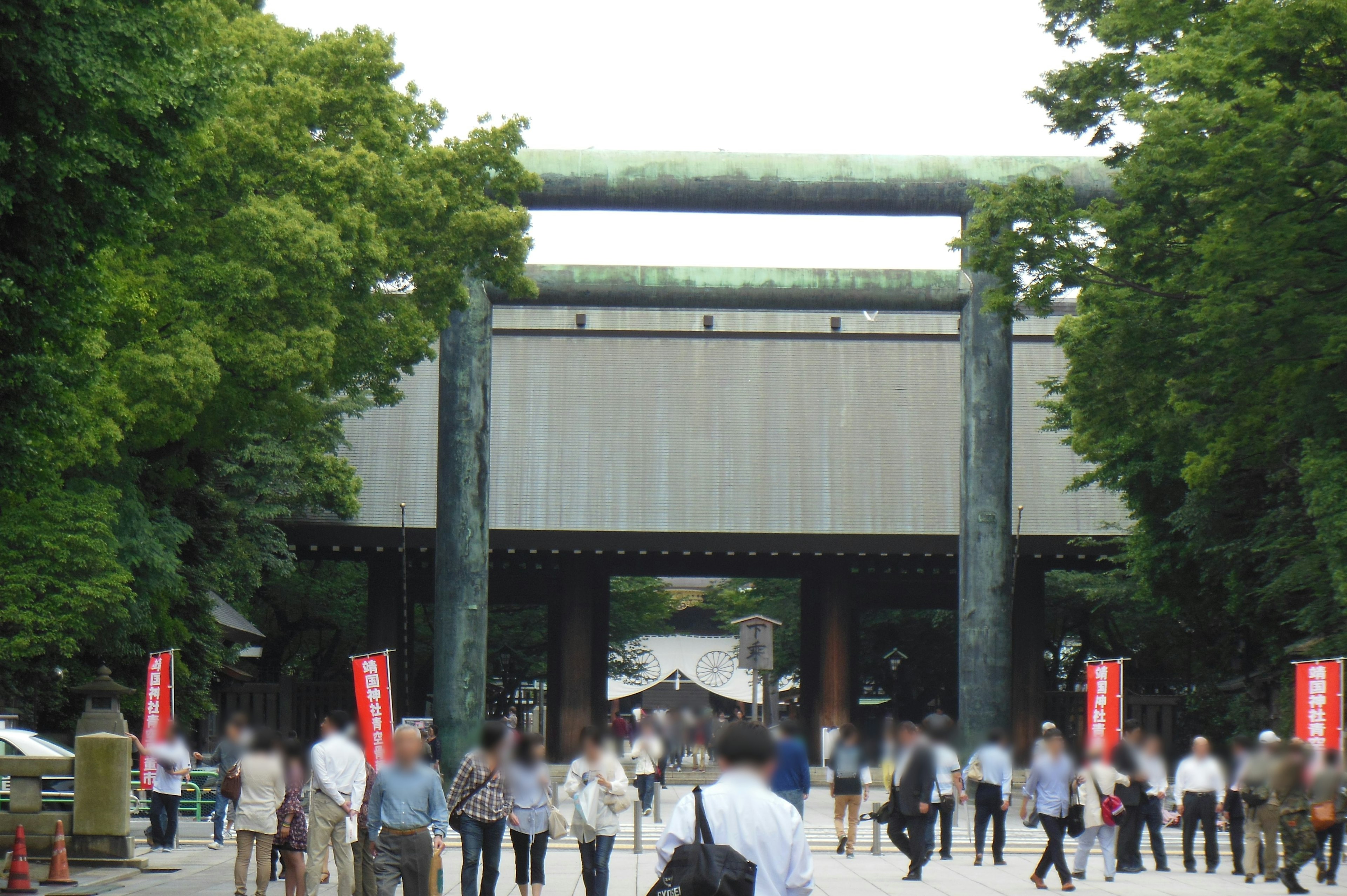 A crowd of people walking through a large torii gate surrounded by lush green trees