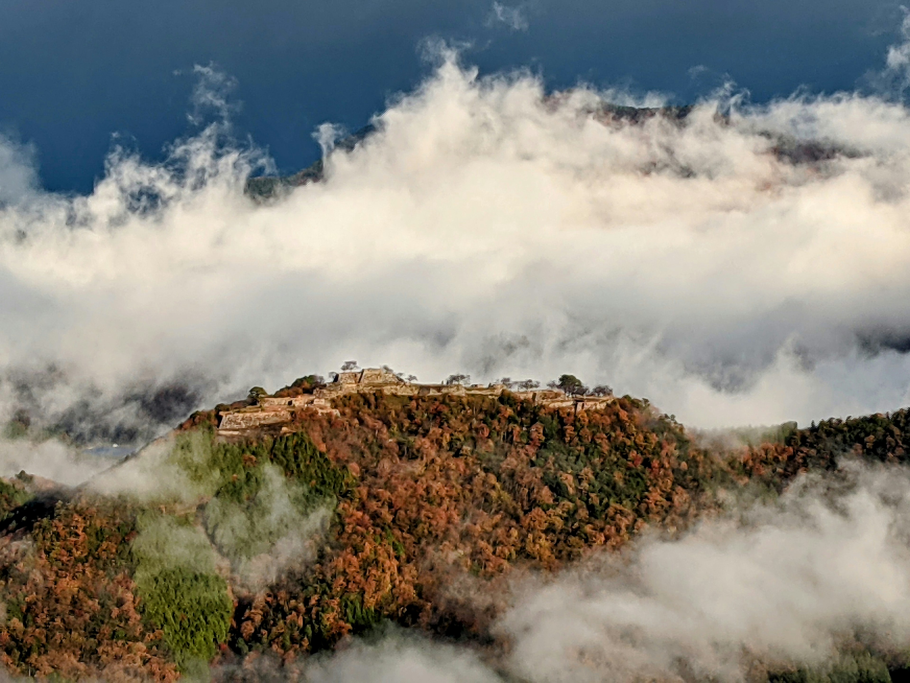 Ruines anciennes au sommet d'une montagne entourées de feuillage d'automne et de nuages