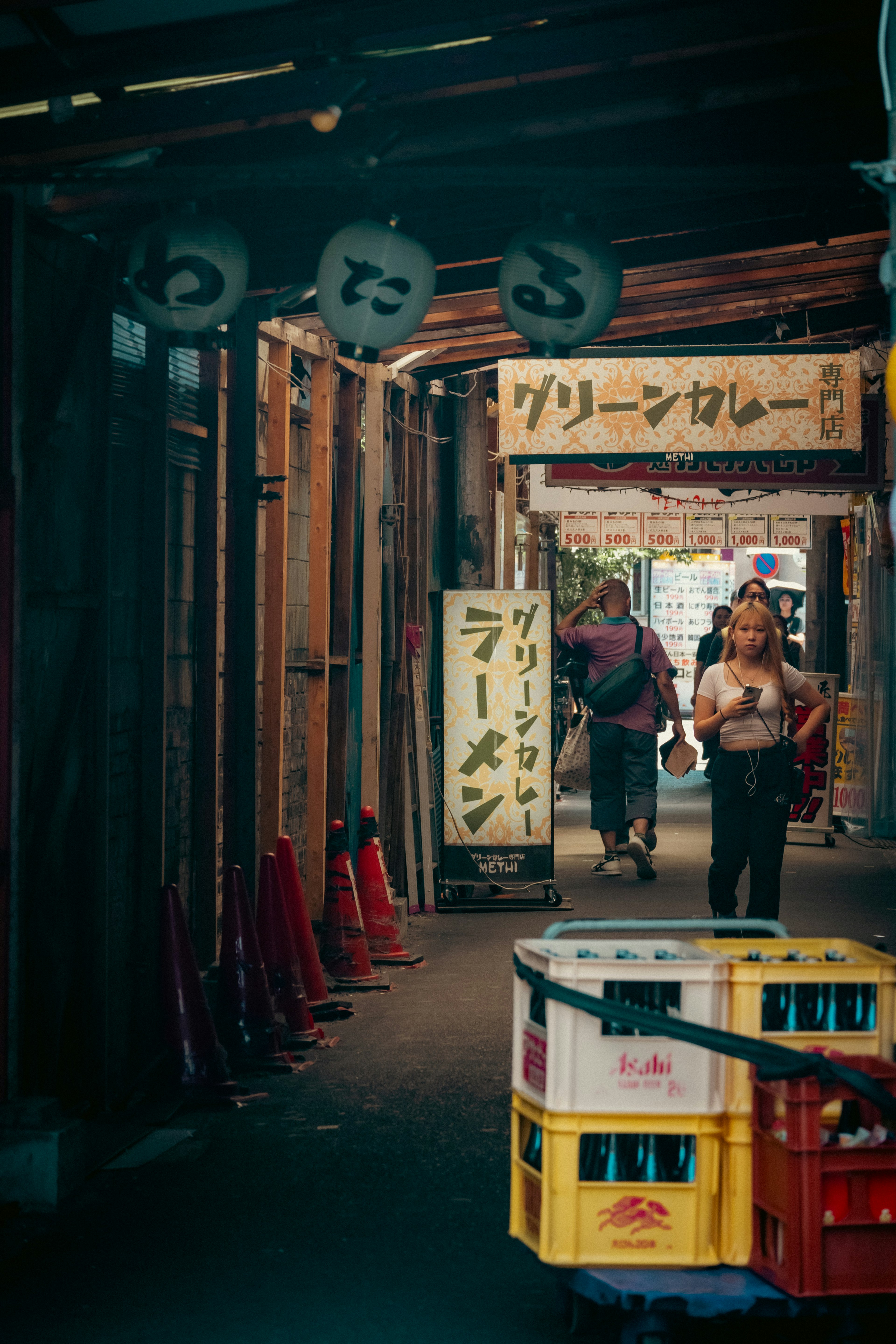 狭い路地に並ぶ看板と色とりどりの箱を持った人