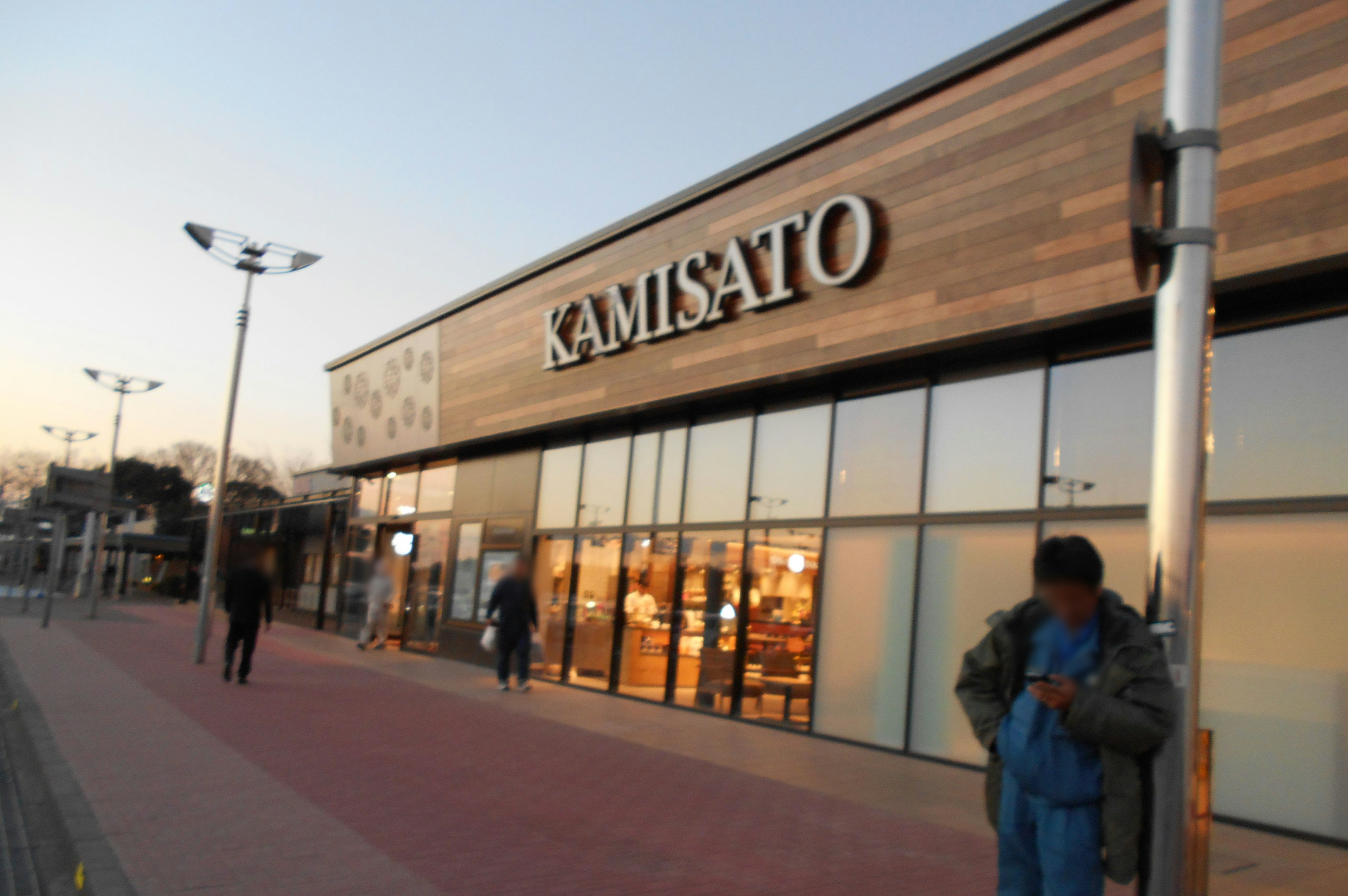 Extérieur du magasin Kamisato au crépuscule avec des piétons sur le trottoir