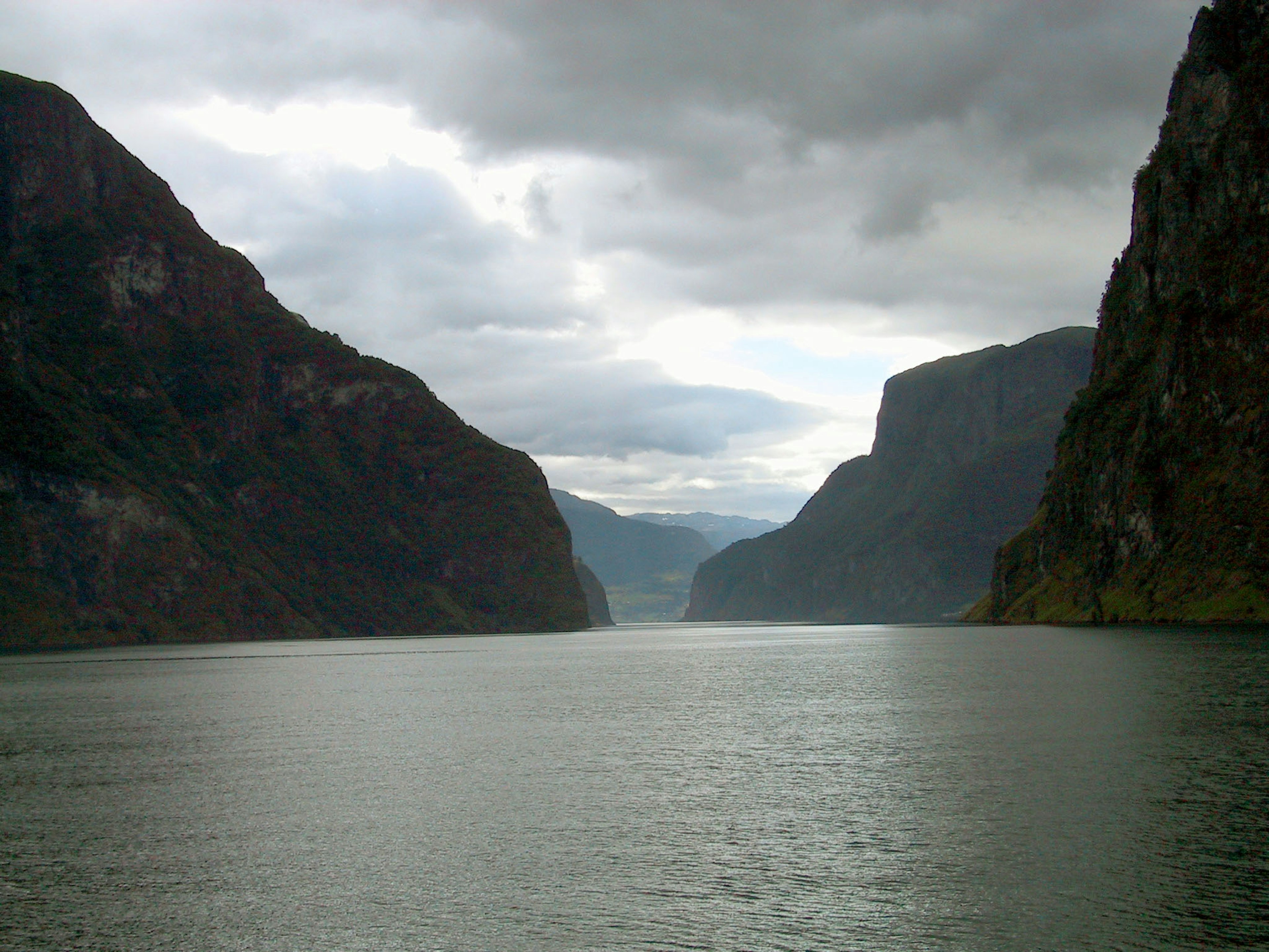 Pemandangan fjord berkabut dengan gunung curam di kedua sisi dan permukaan air tenang