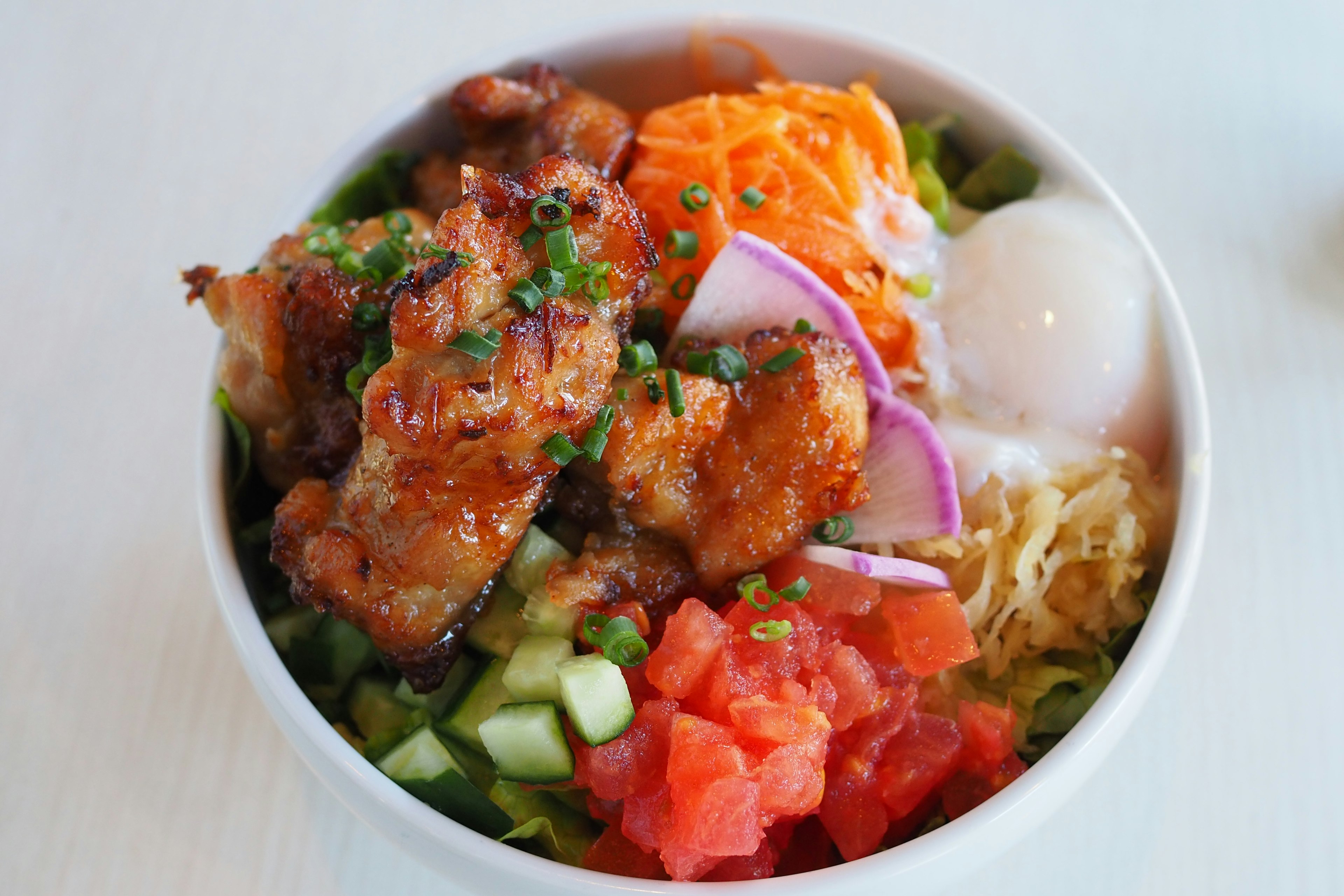 Bowl of chicken and vegetables topped with egg and tomato salad