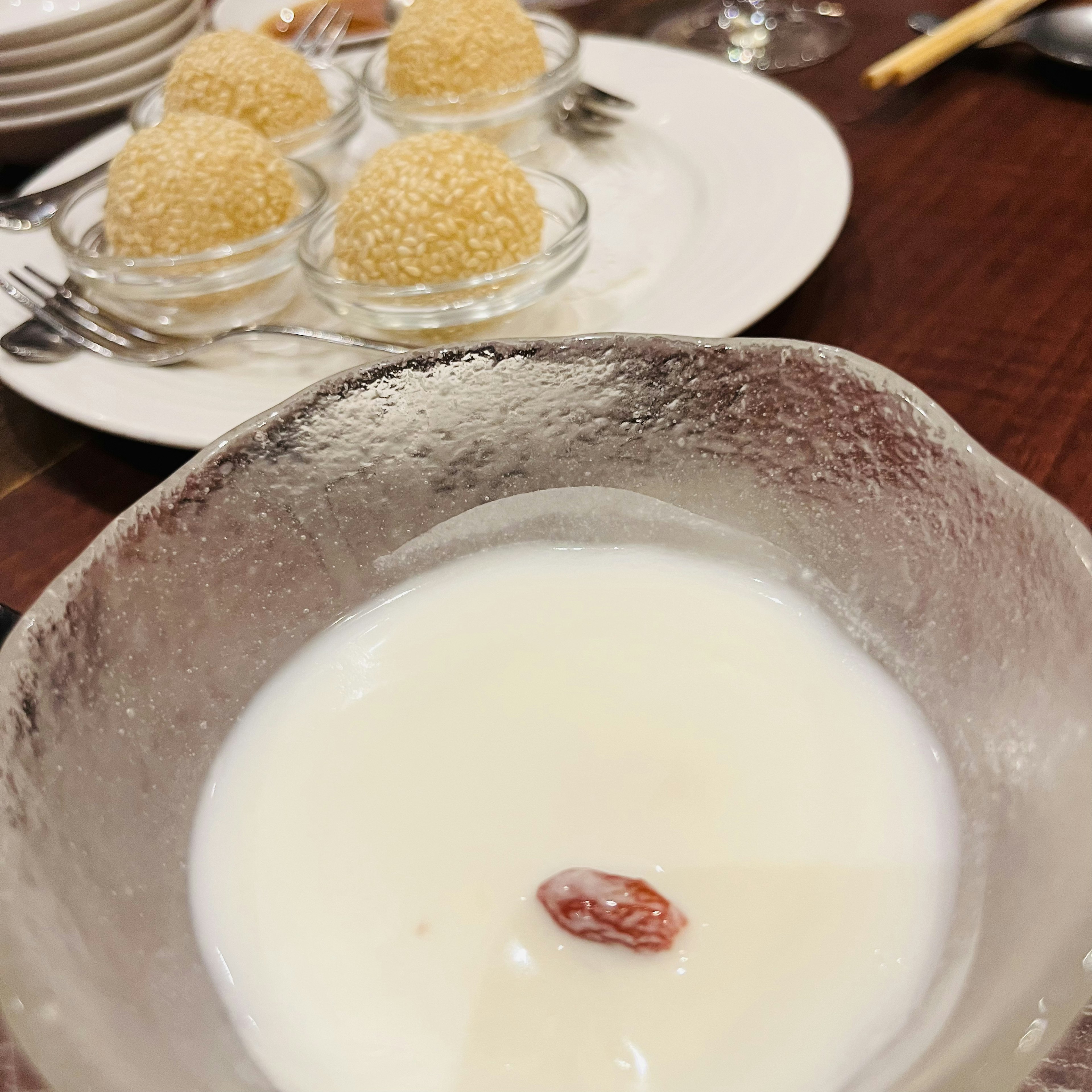 Postre con sopa blanca que presenta una baya de goji y cuatro bolas de sésamo al fondo