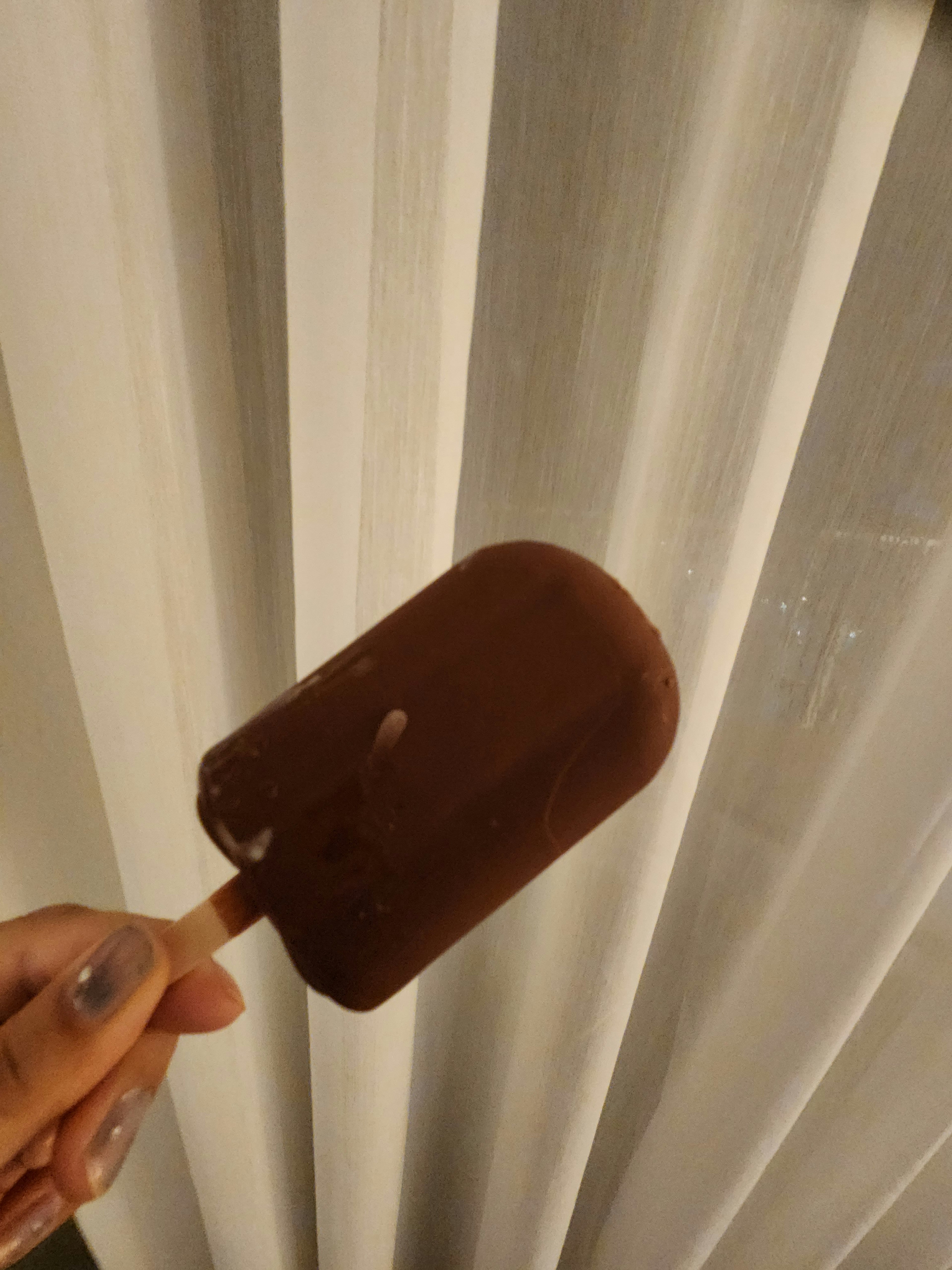 Mano che tiene un gelato al cioccolato con sfondo di tende