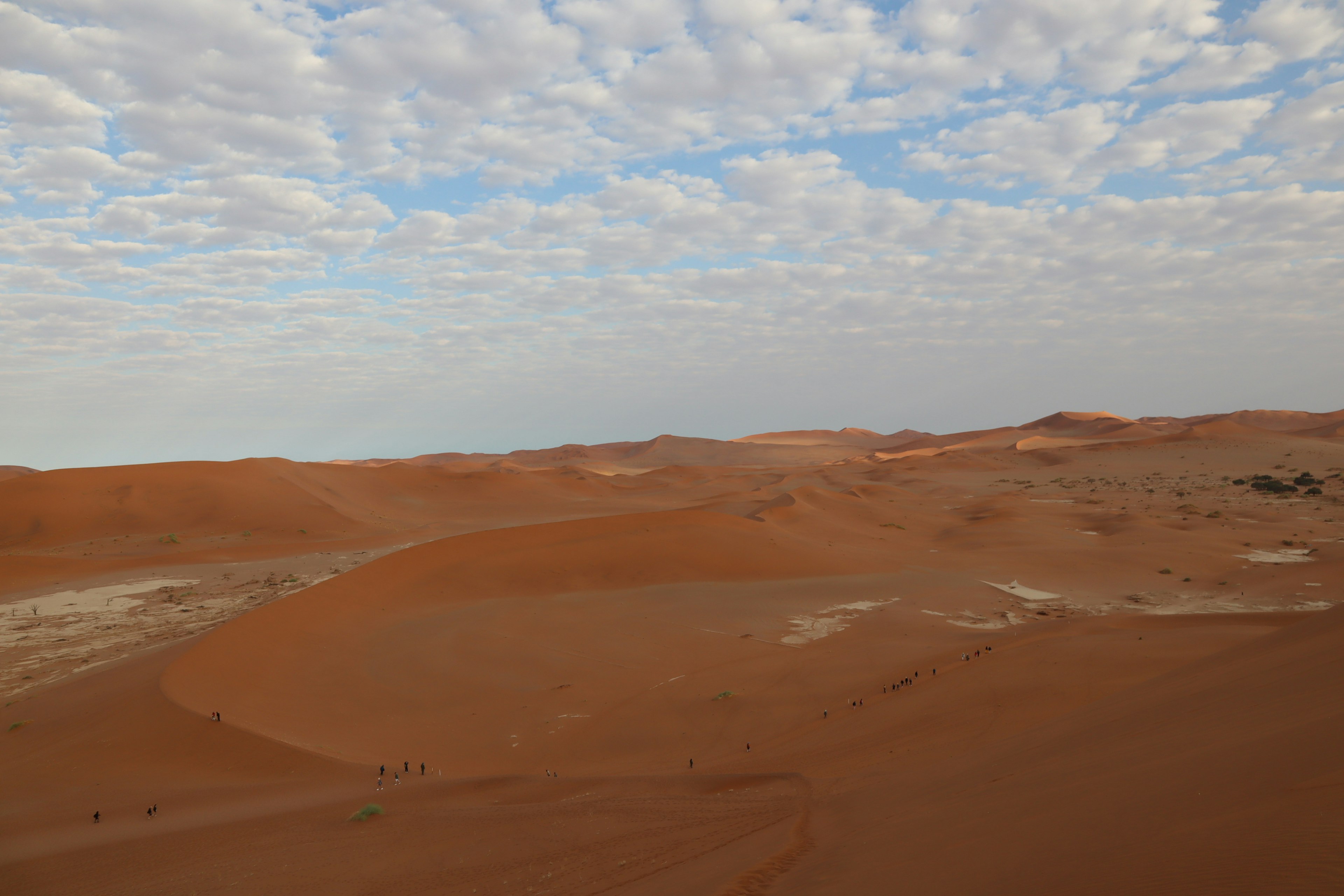 Vast desert landscape with orange dunes and blue sky filled with clouds