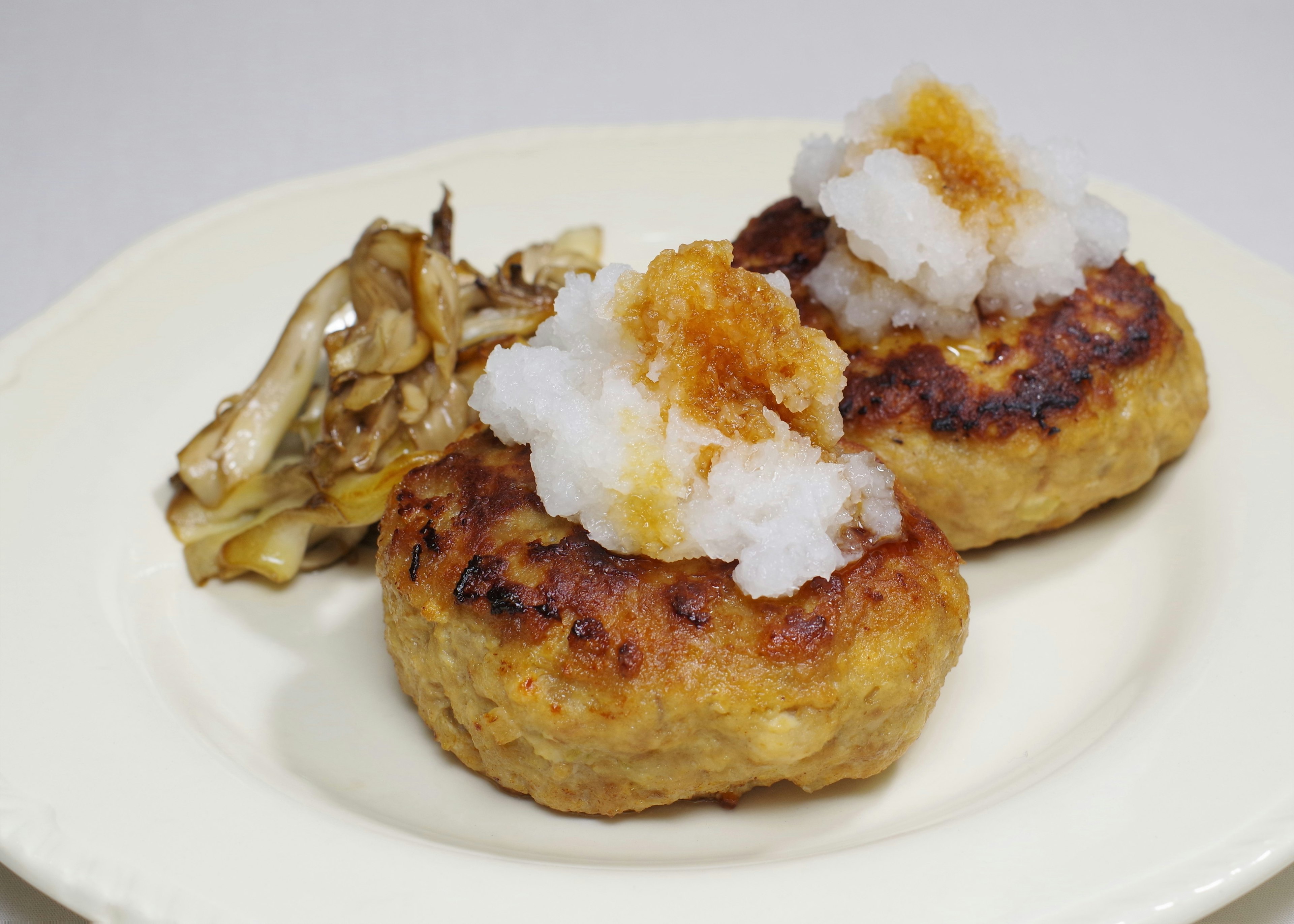 Two hamburger patties topped with grated daikon radish served with a side of mushrooms