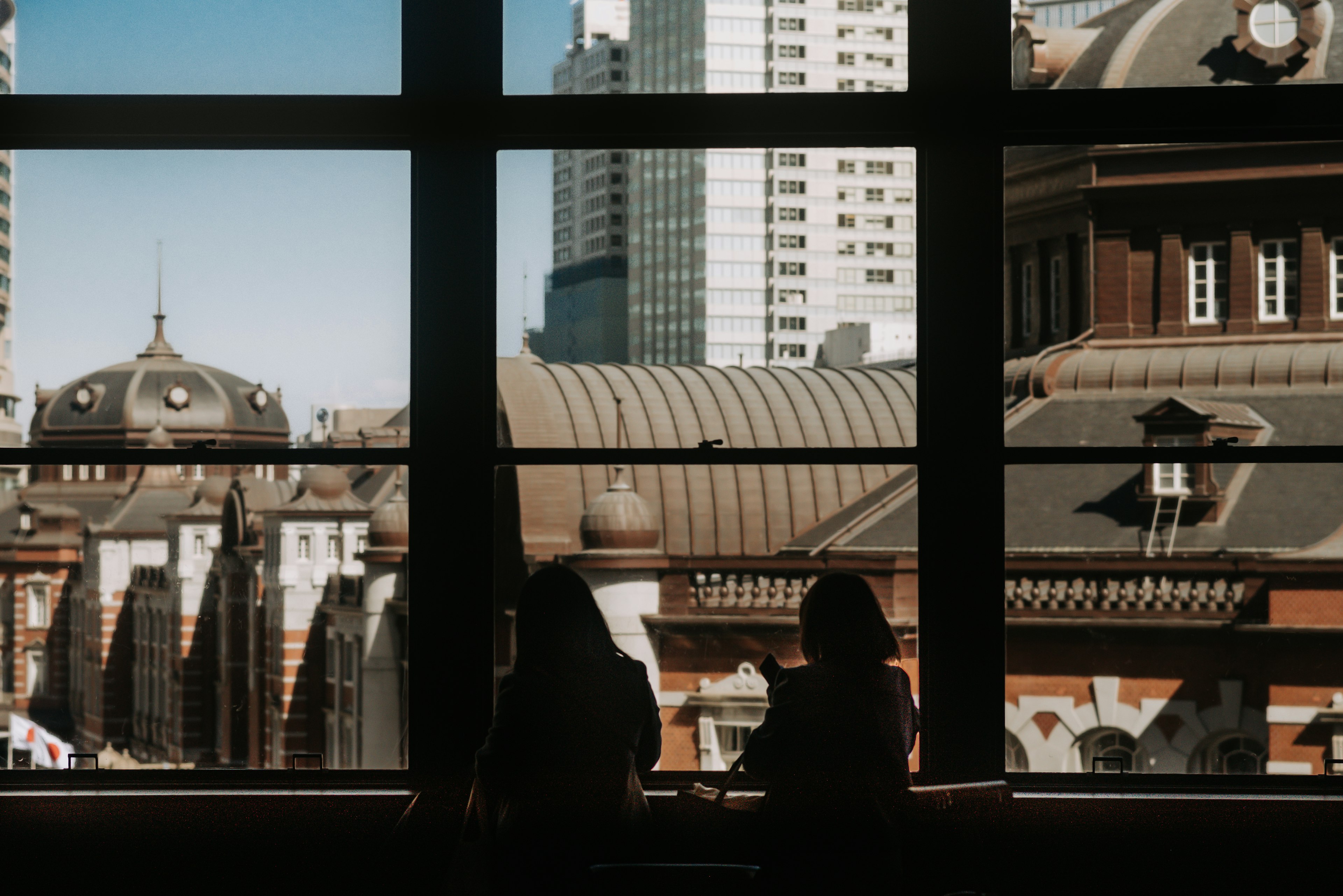 Silhouettes of two people looking out at cityscape through a window