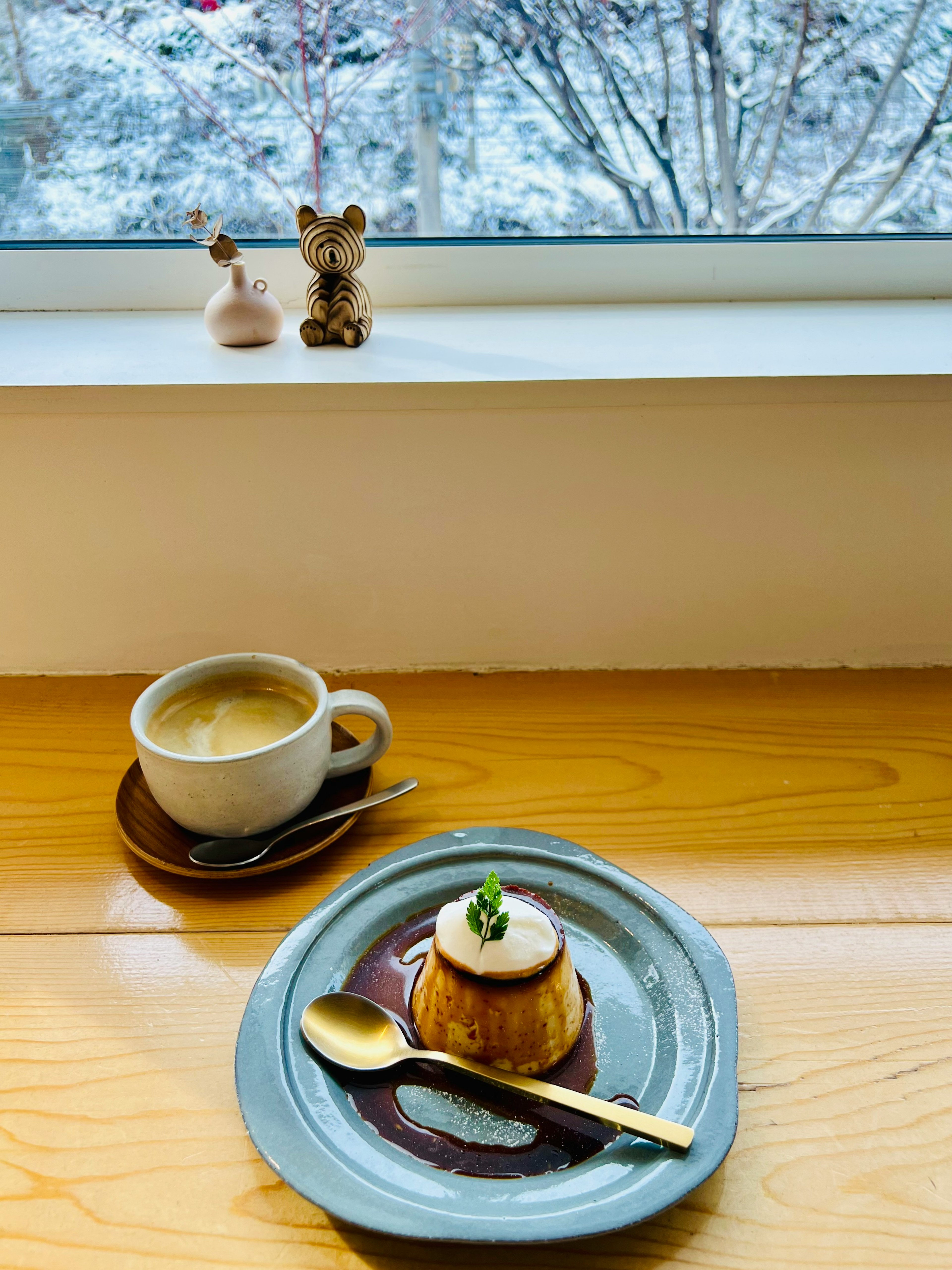 Tasse Kaffee und Dessertteller auf einem Holztisch neben einem Fenster mit schneebedecktem Hintergrund