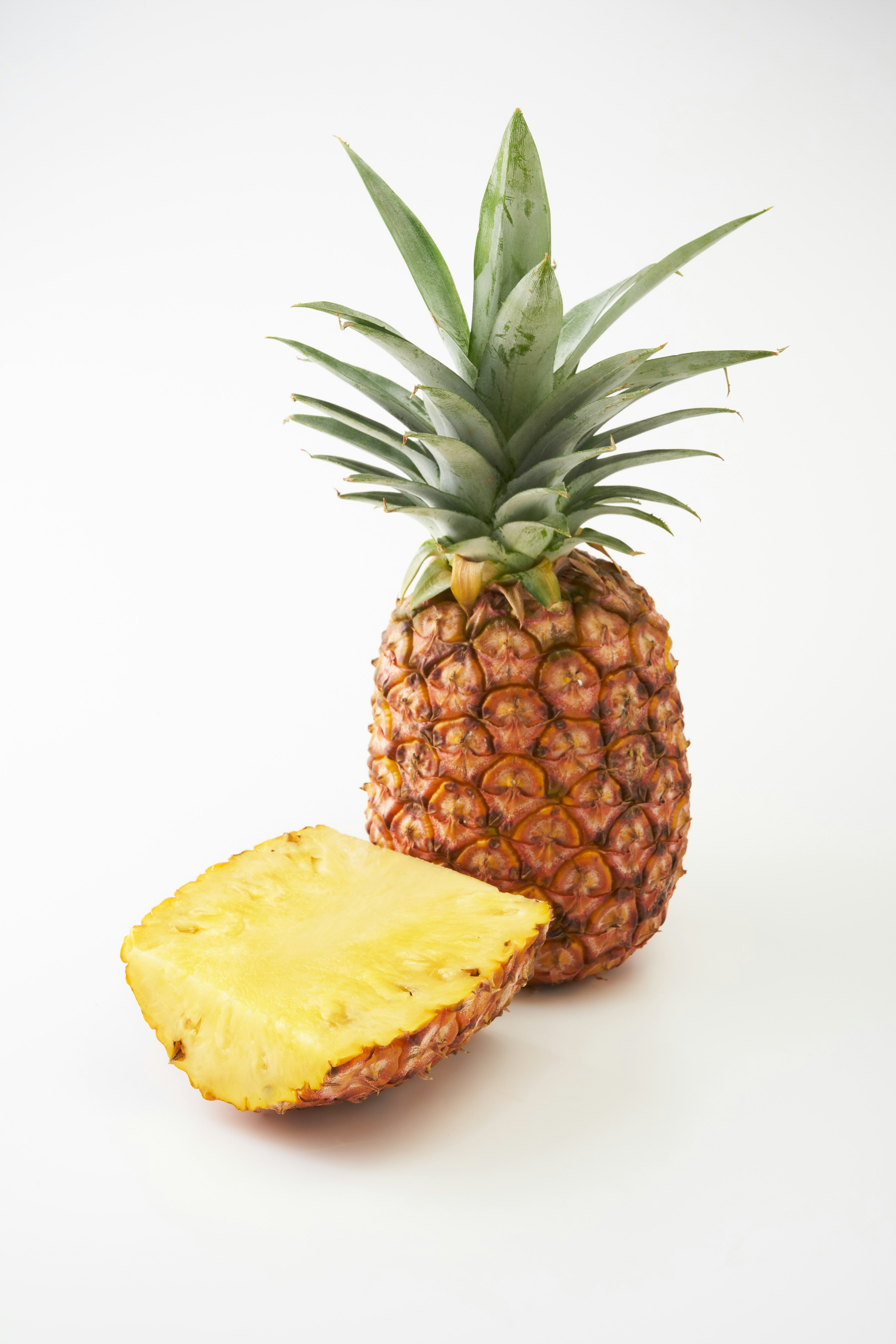 A whole pineapple with a slice cut out sits on a white background