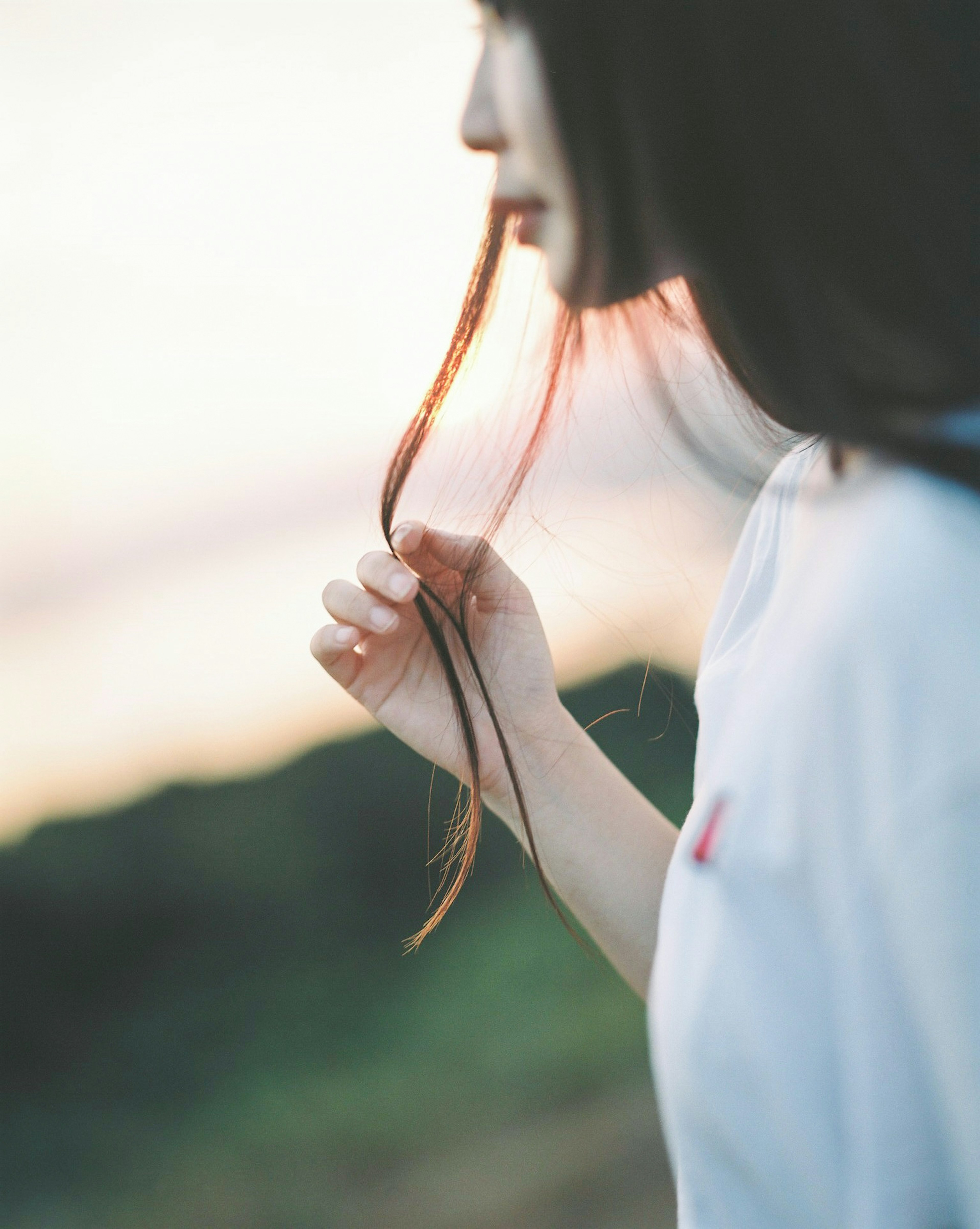 夕暮れ時に髪を引き寄せる女性の横顔