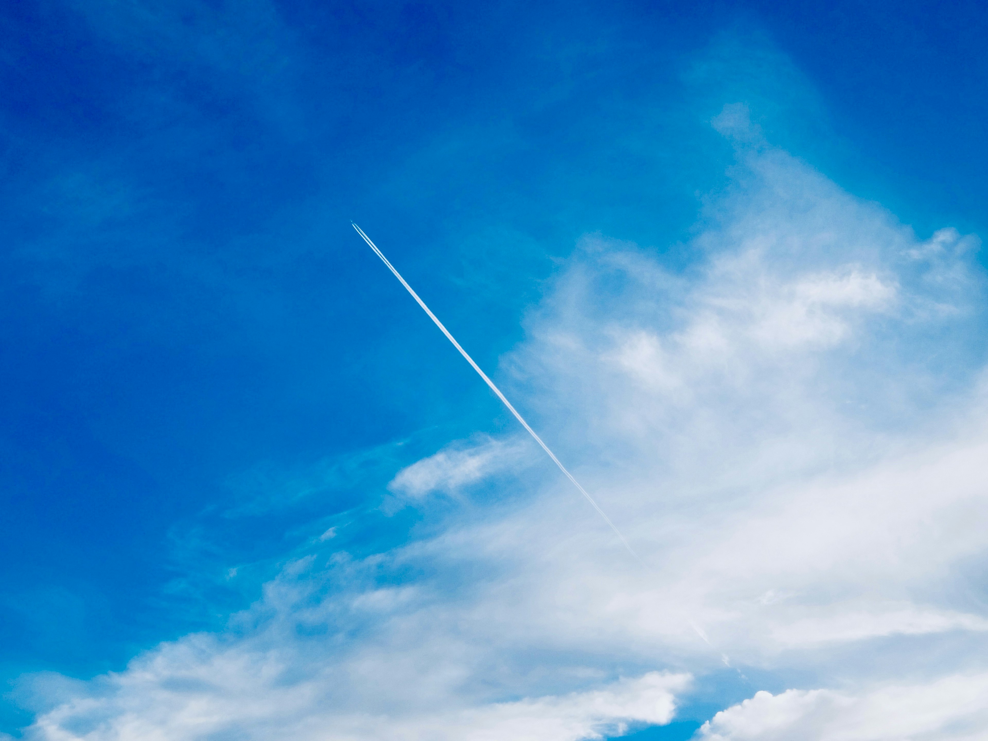 青空に白い飛行機雲が伸びている風景