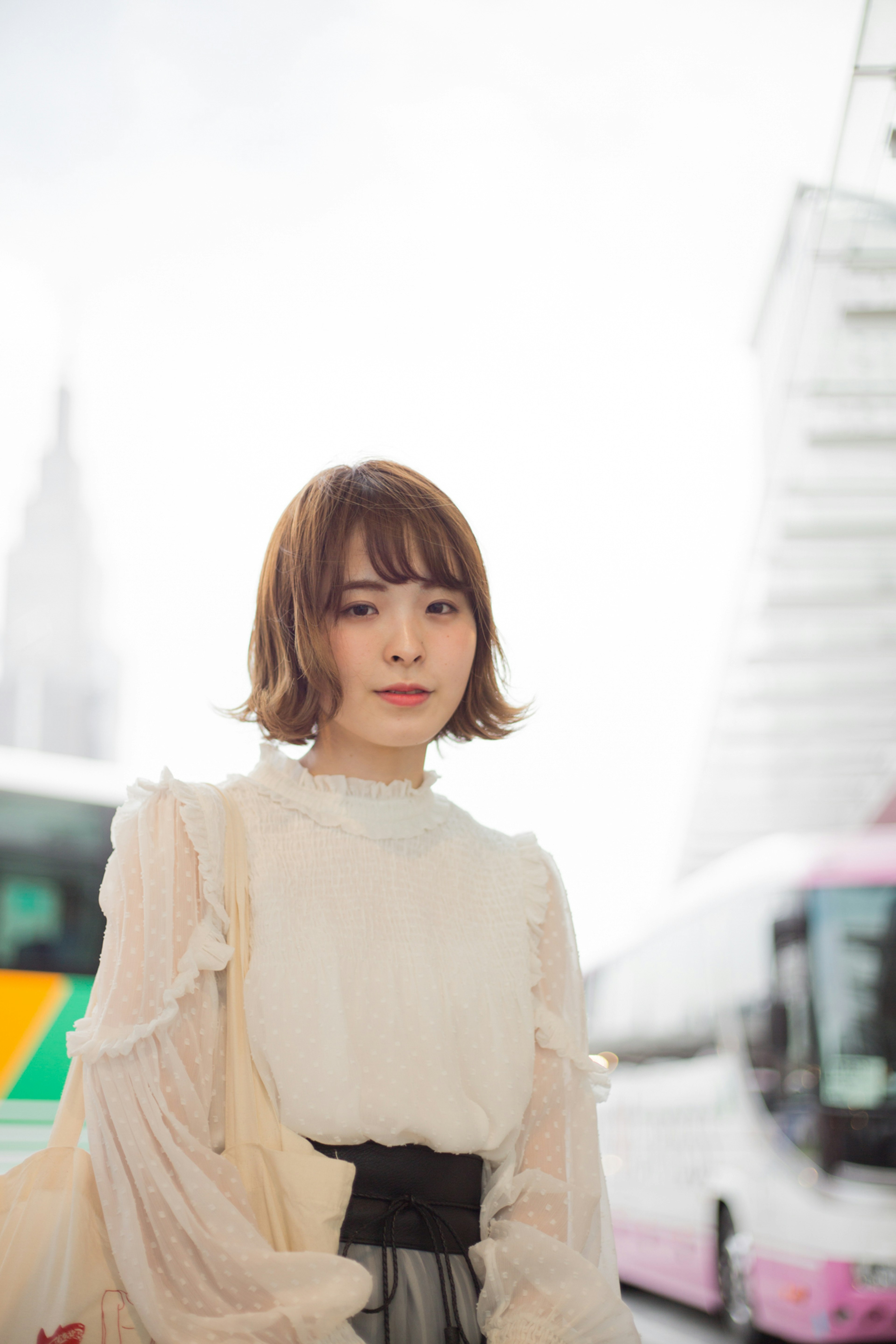 A woman wearing a white blouse stands against a bright background