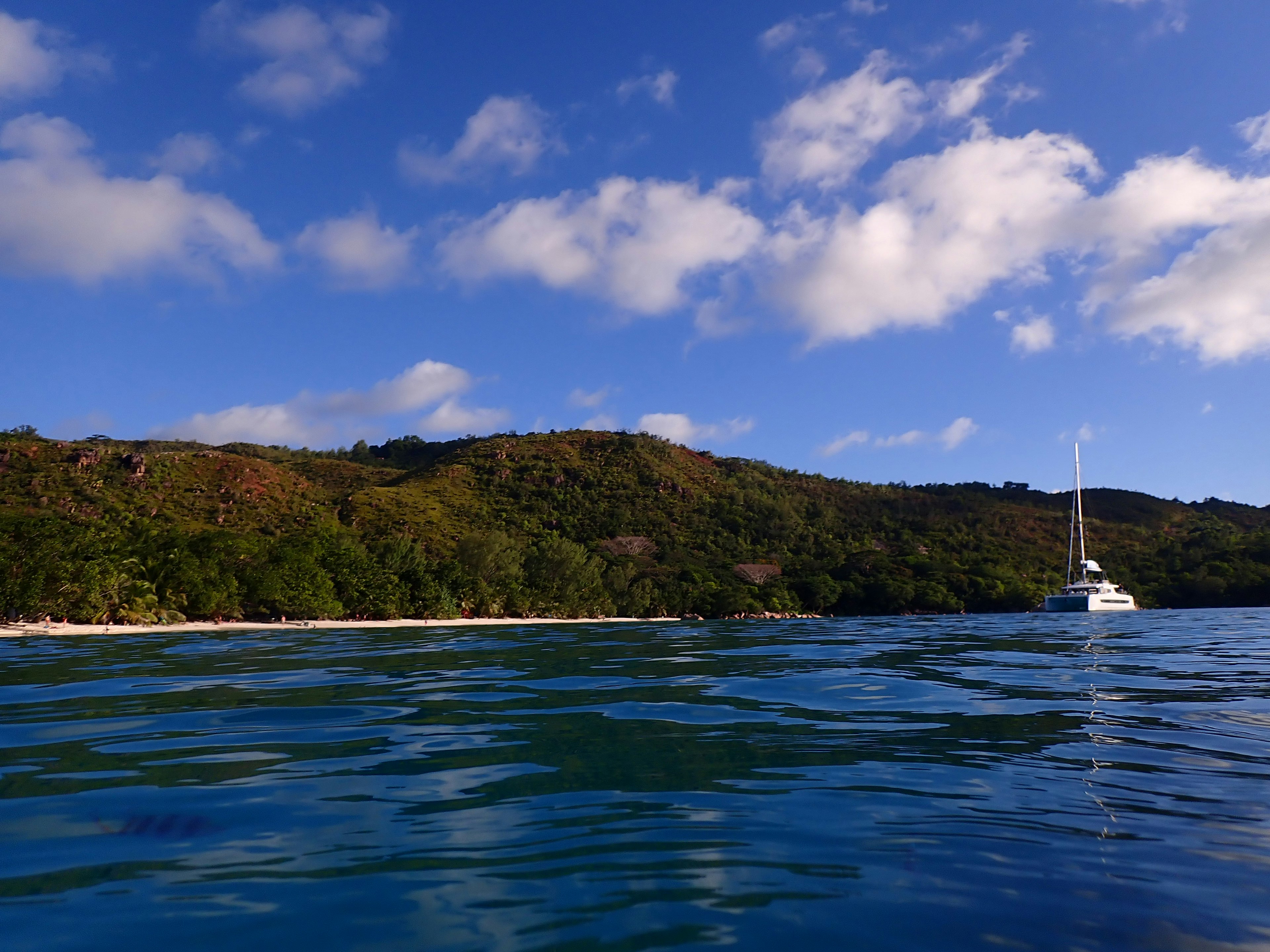 ทิวทัศน์ของเรือยอชท์บนทะเลสีน้ำเงินพร้อมภูเขาสีเขียวด้านหลัง