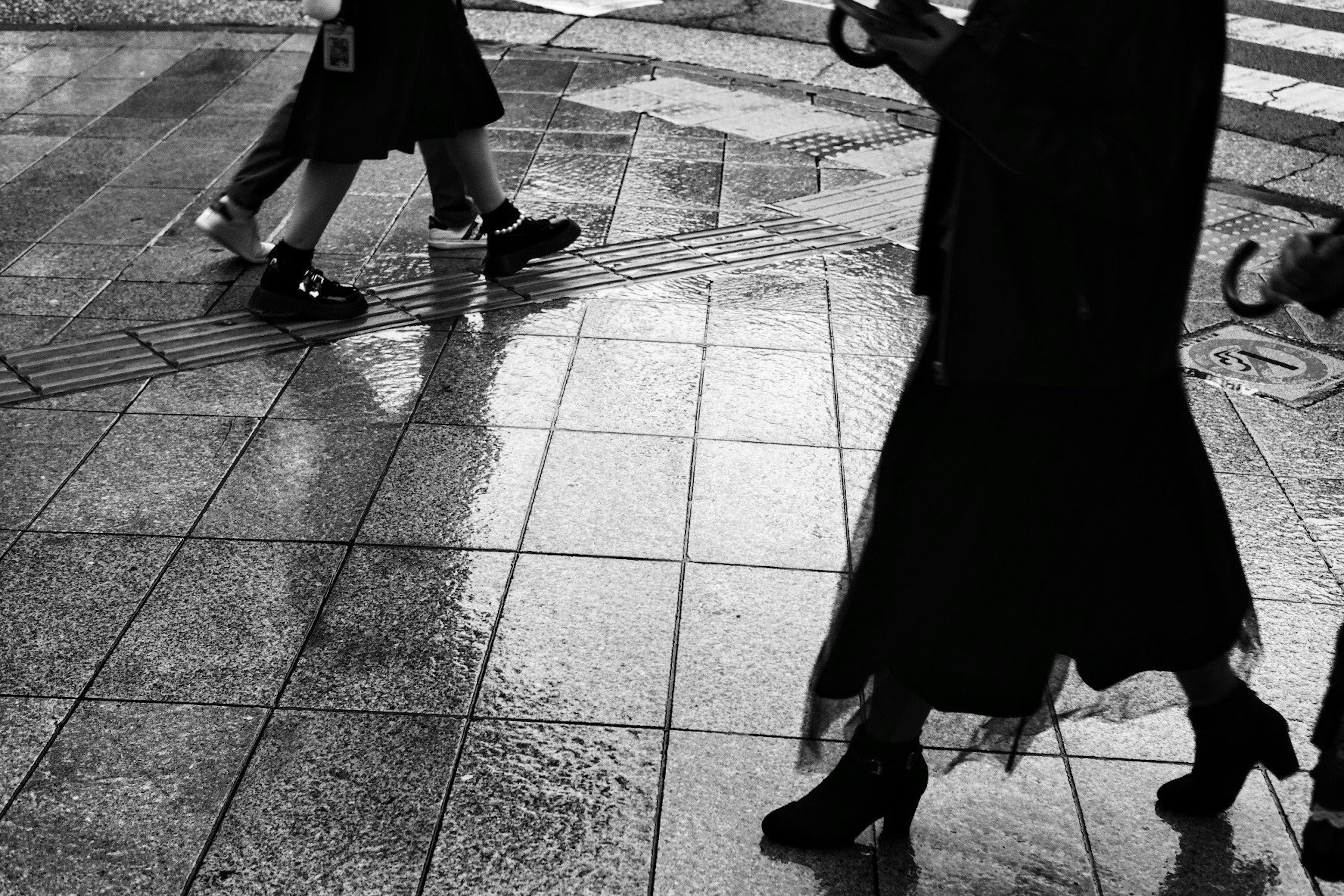 雨に濡れたタイルの上を歩く人々の影