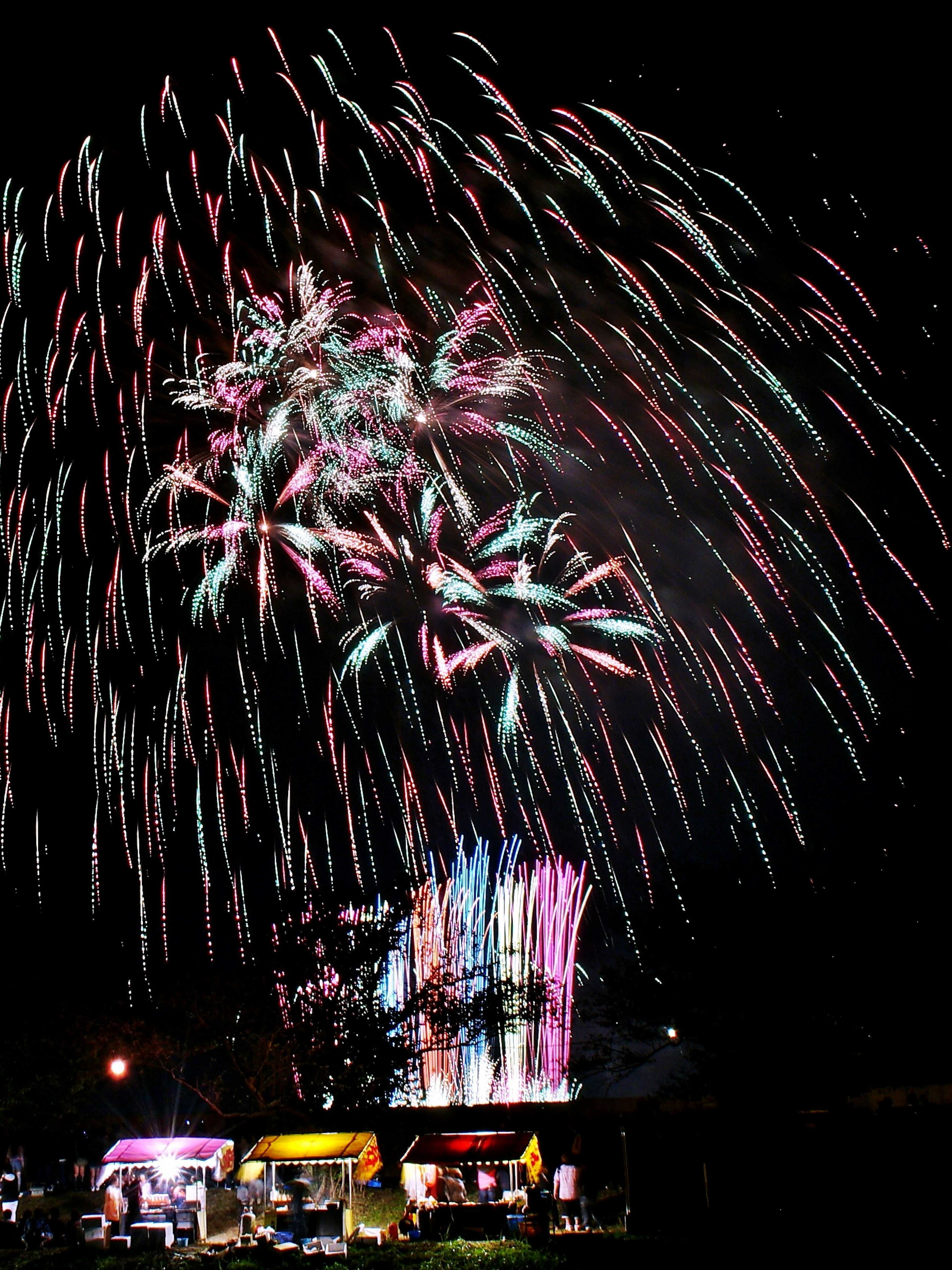 Colorful fireworks exploding in the night sky with food stalls below