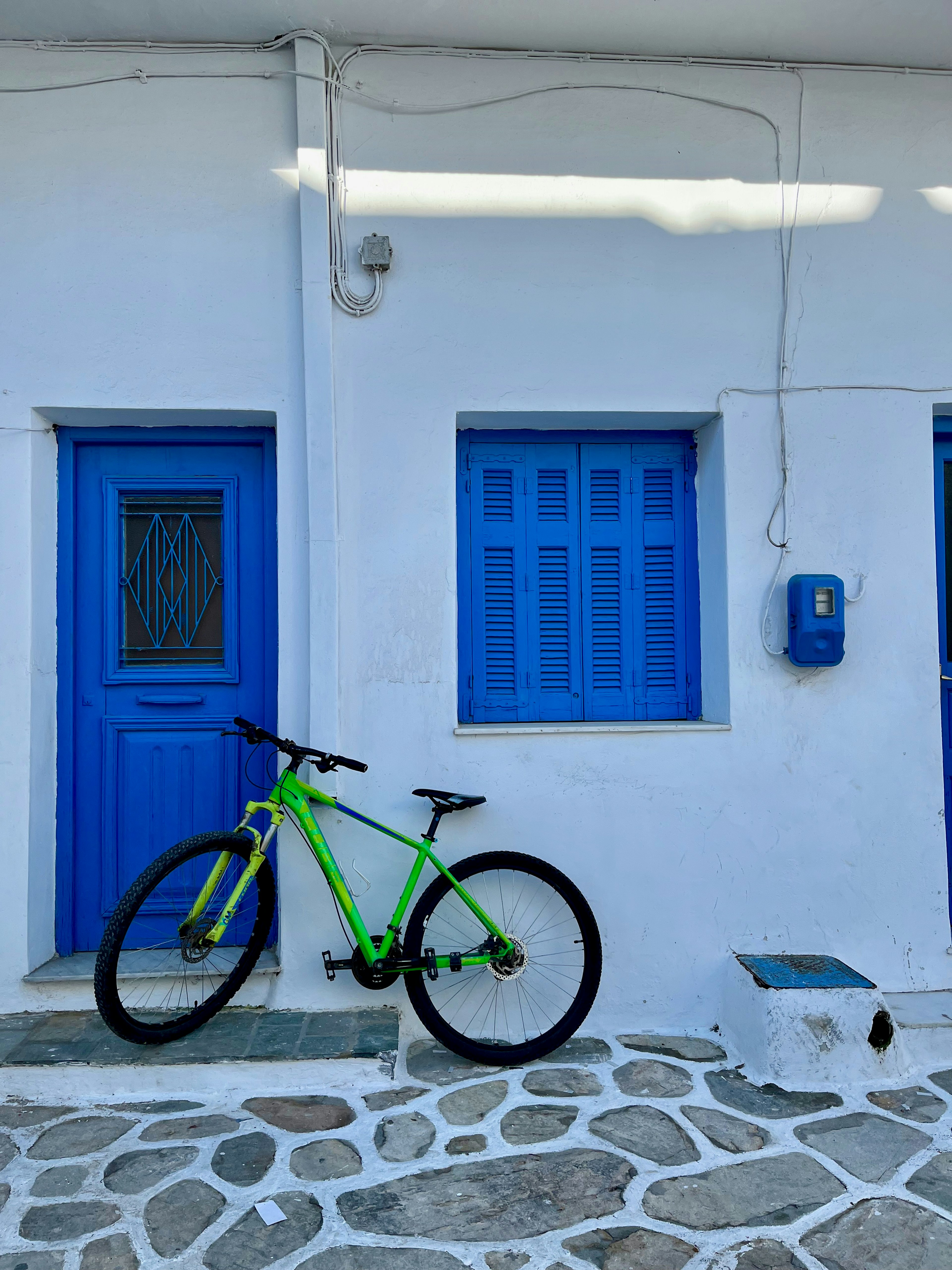 Green bicycle leaning against white wall with blue doors