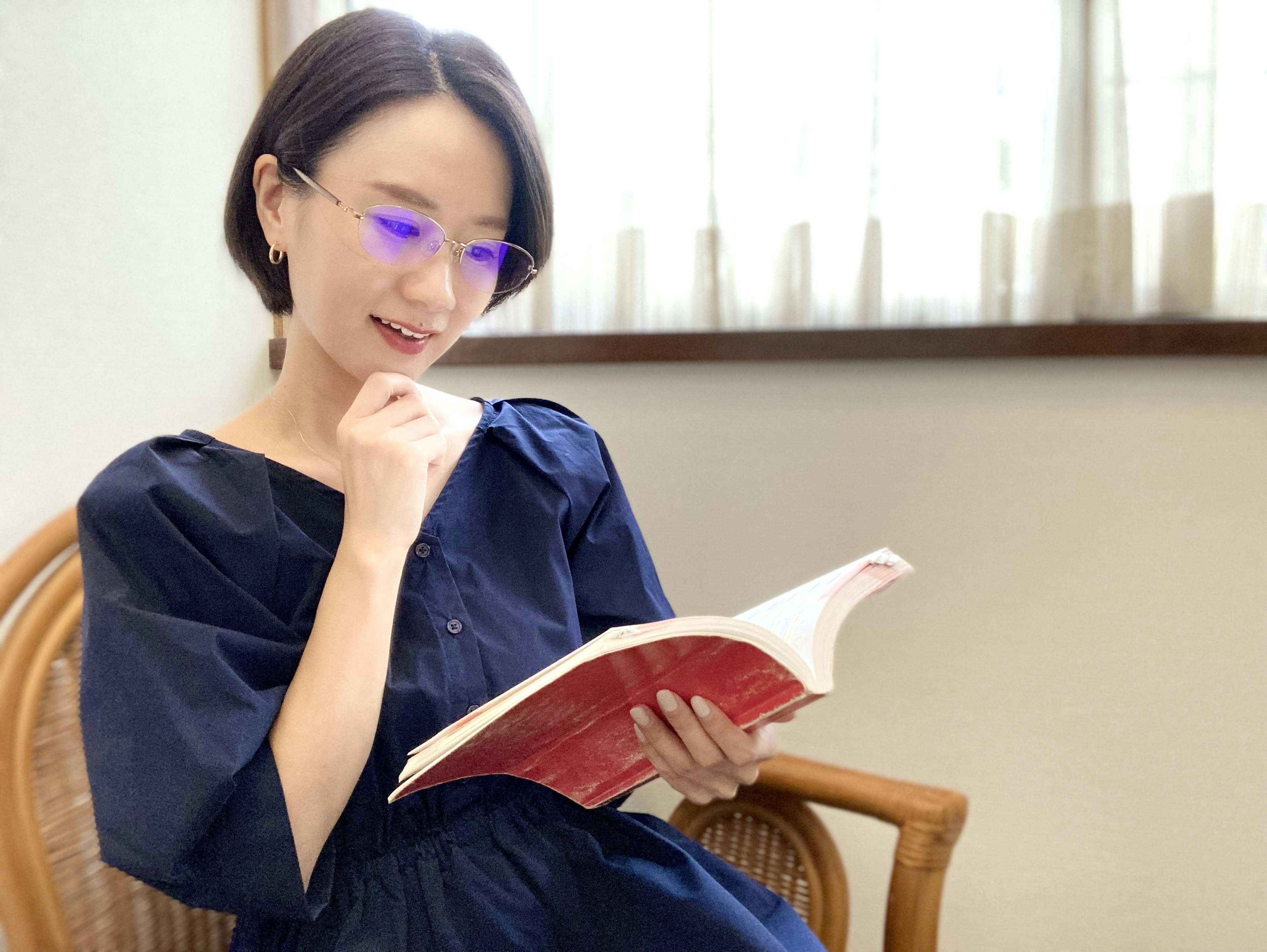 Femme lisant un livre près de la fenêtre, portant des lunettes bleues, lumière naturelle