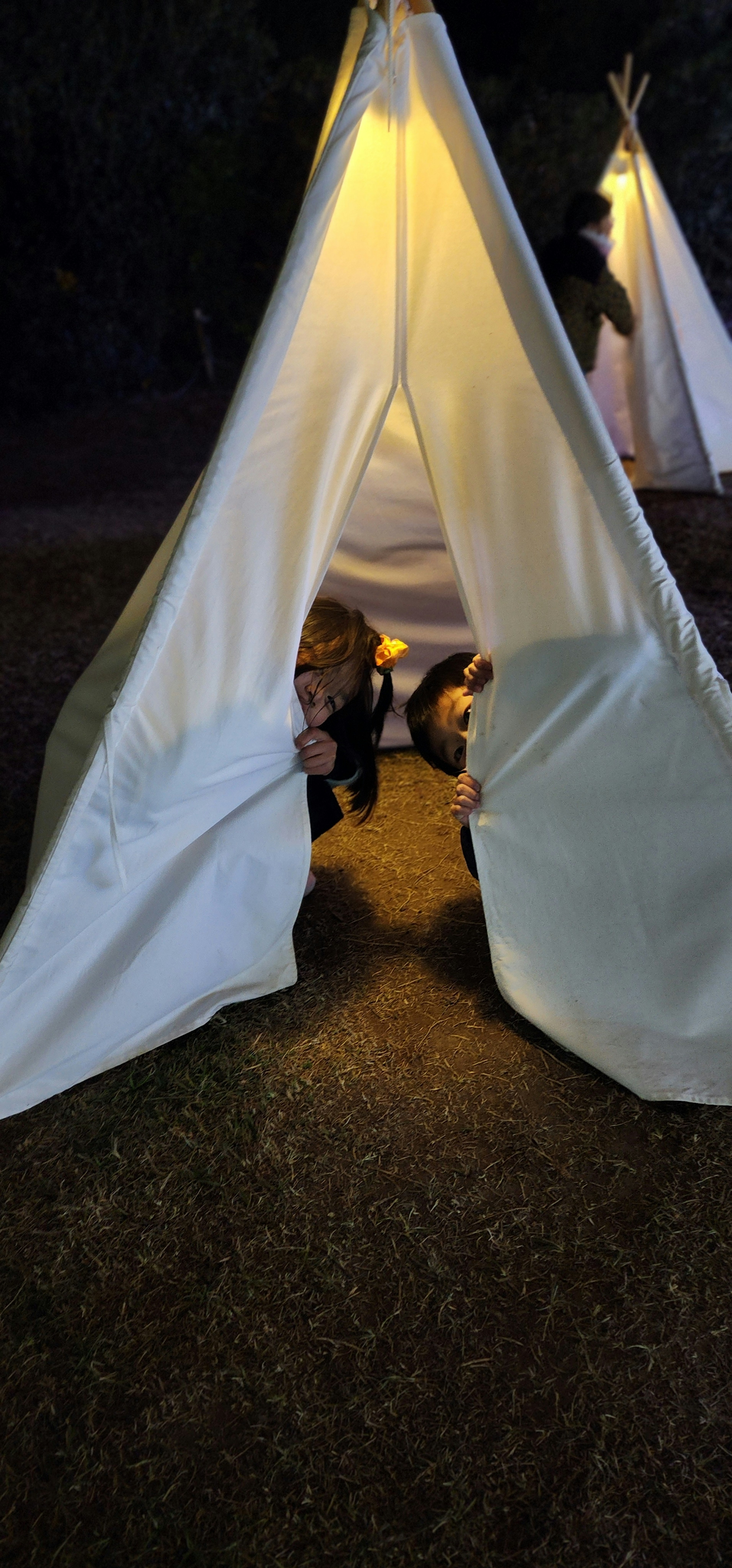 Children peeking out from a lit tent at night