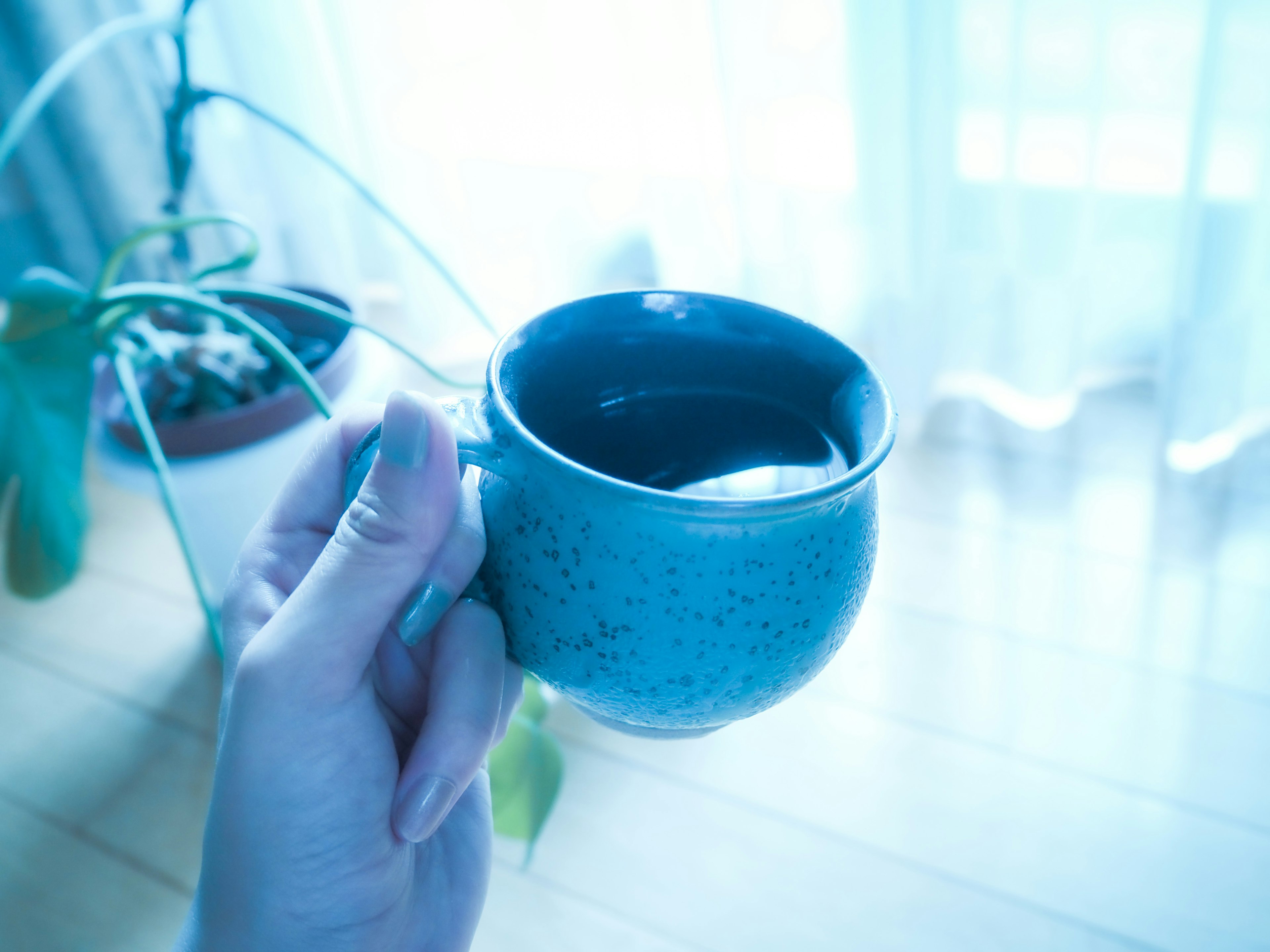 Primer plano de una mano sosteniendo una taza de cerámica azul cerca de una ventana iluminada por el sol