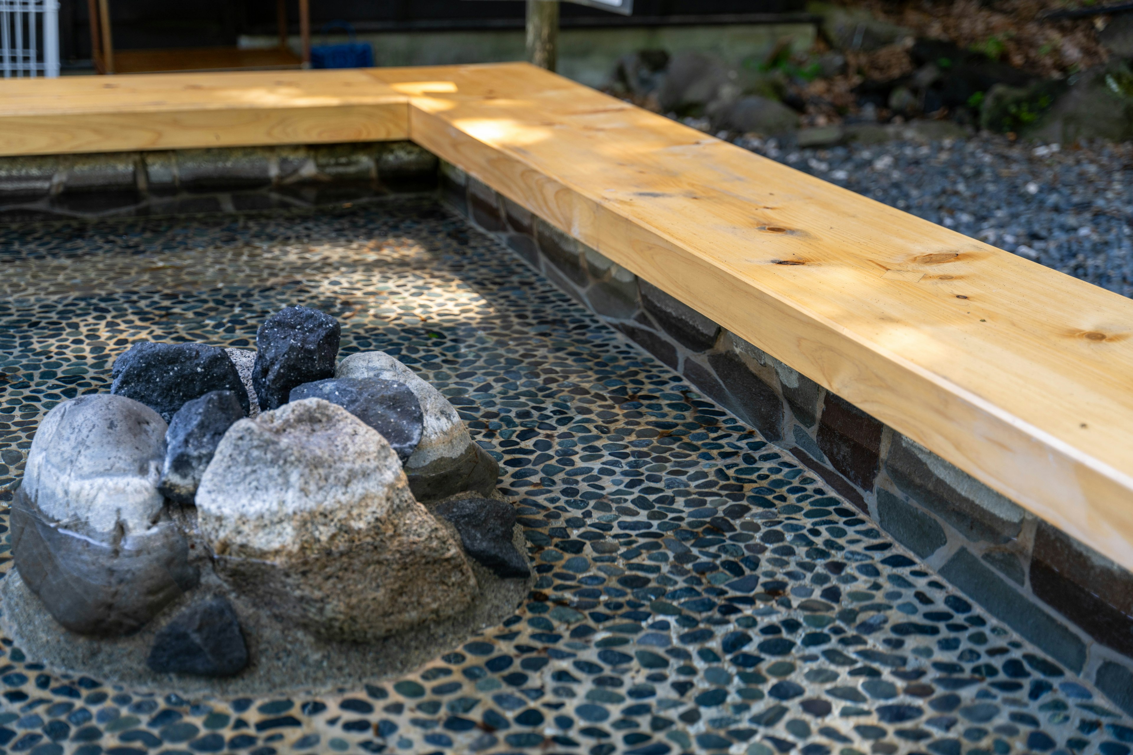 Fogata de piedra con borde de madera y jardín de guijarros