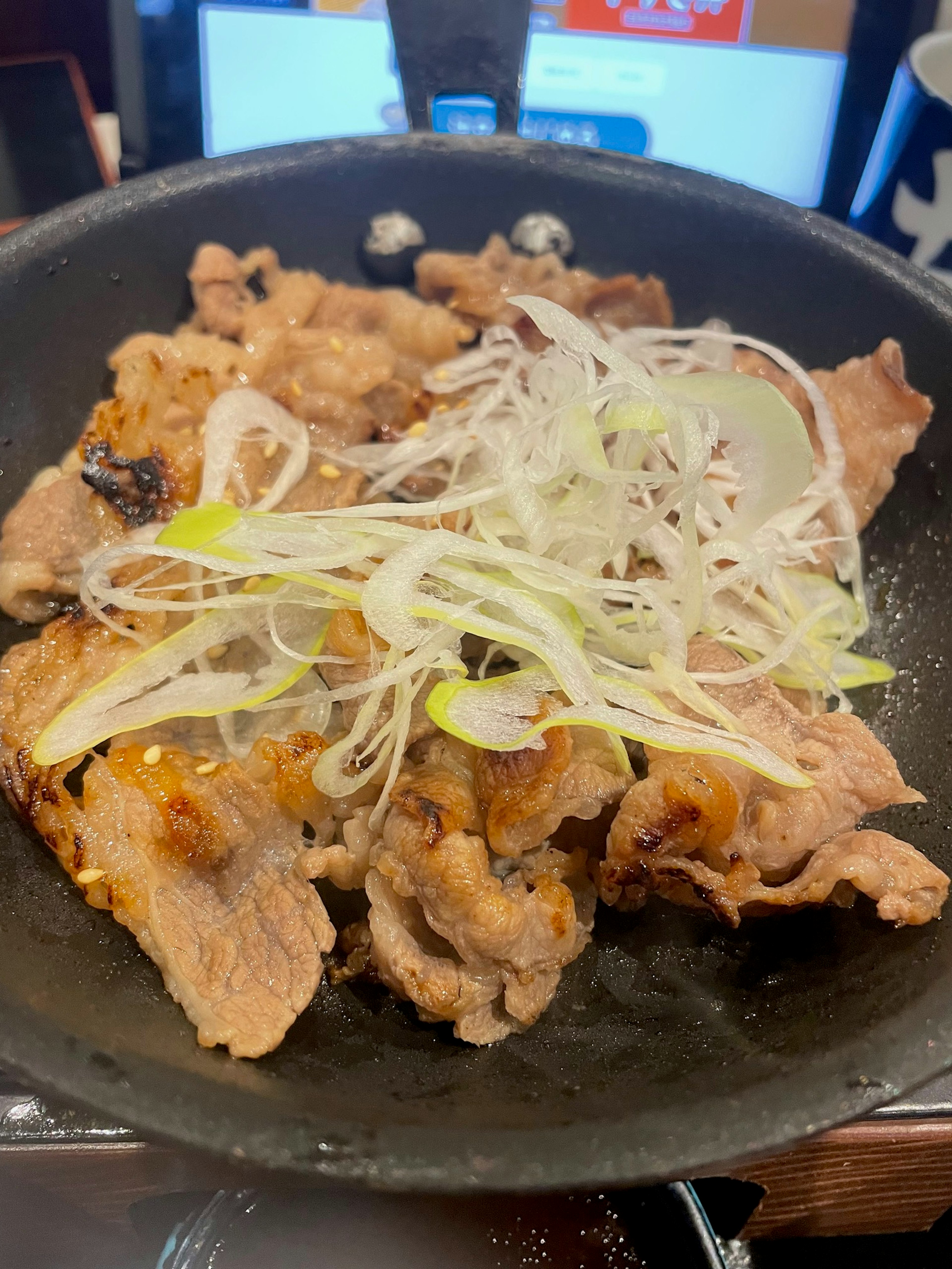 Sizzling pork dish topped with green onions in a black frying pan