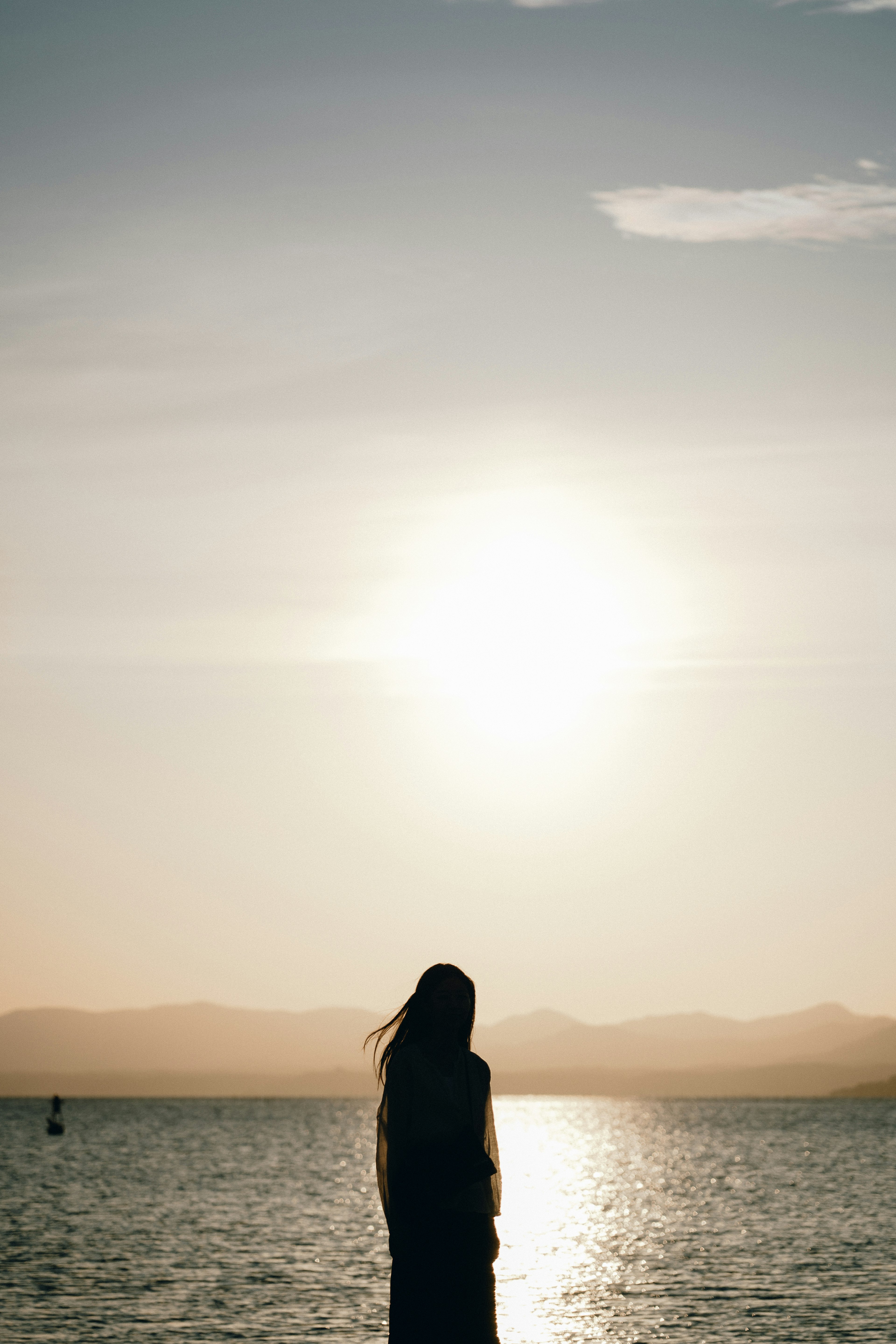 Silhouette einer Frau, die am Meer steht mit Sonnenuntergangslicht