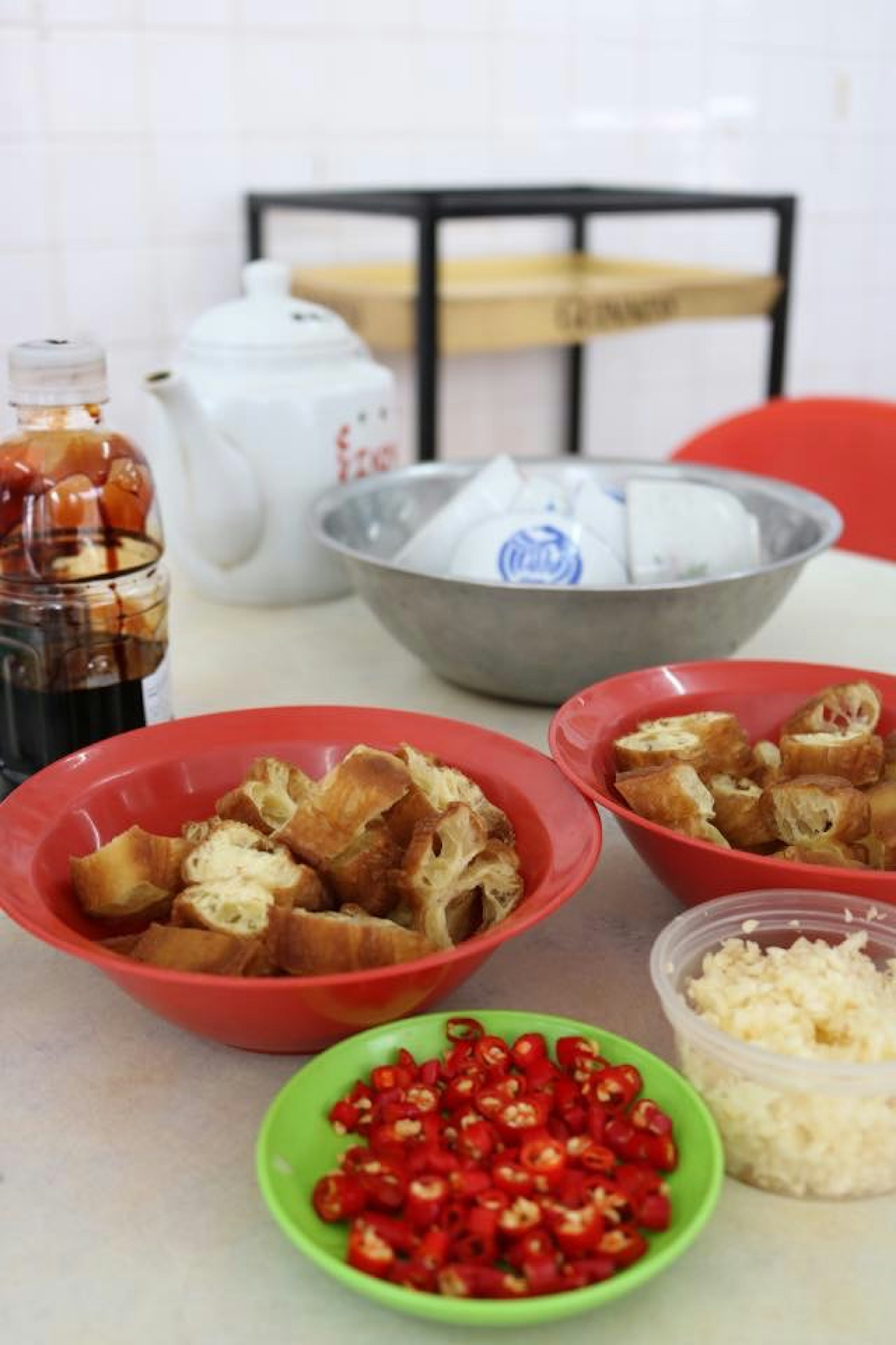 Una escena de comida con pan frito en platos rojos y chiles picados en un plato verde sobre una mesa