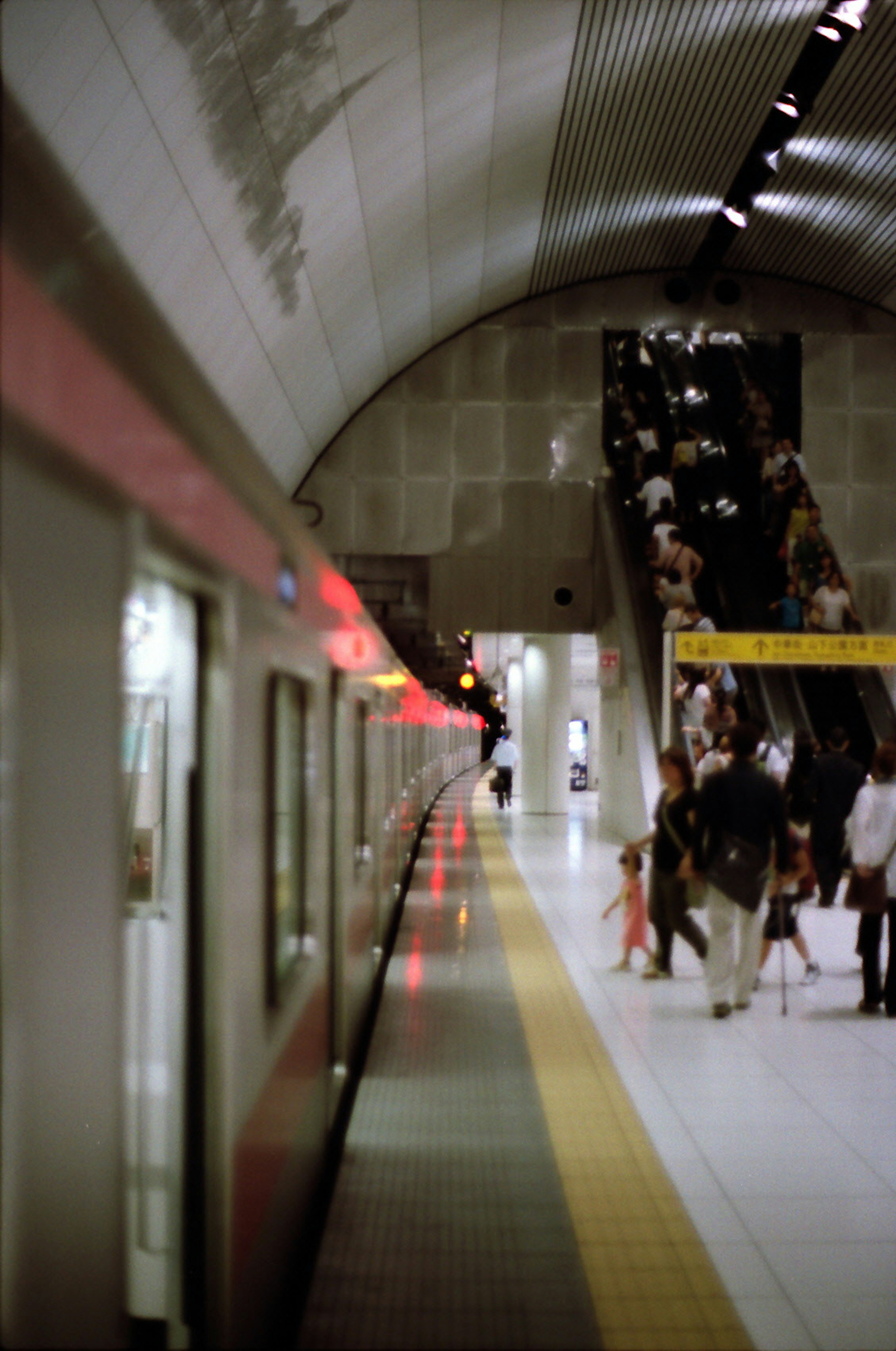 Subway platform with a stopped train and passengers using the escalator