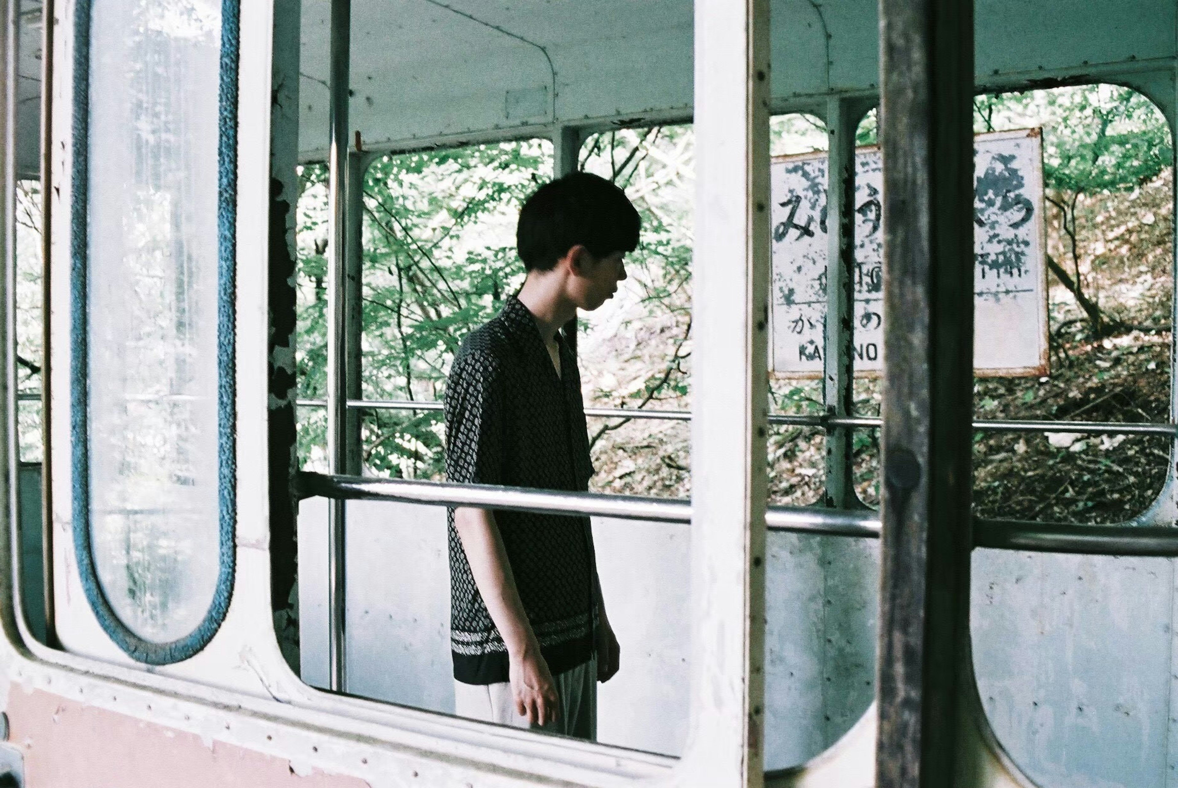 A young man standing inside an abandoned trolleybus with foliage outside