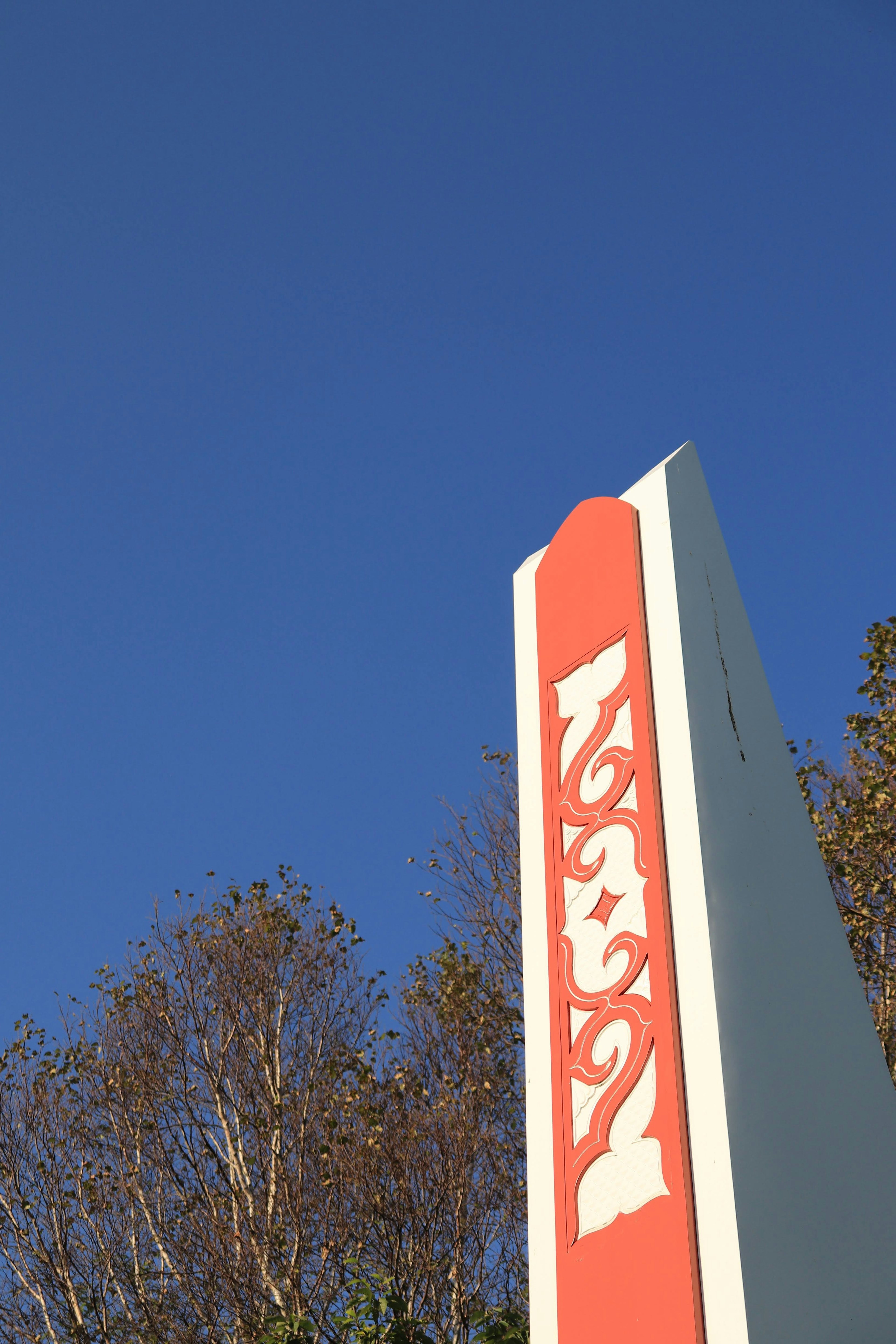 An object partially visible against a blue sky featuring a gray pillar with orange decorations