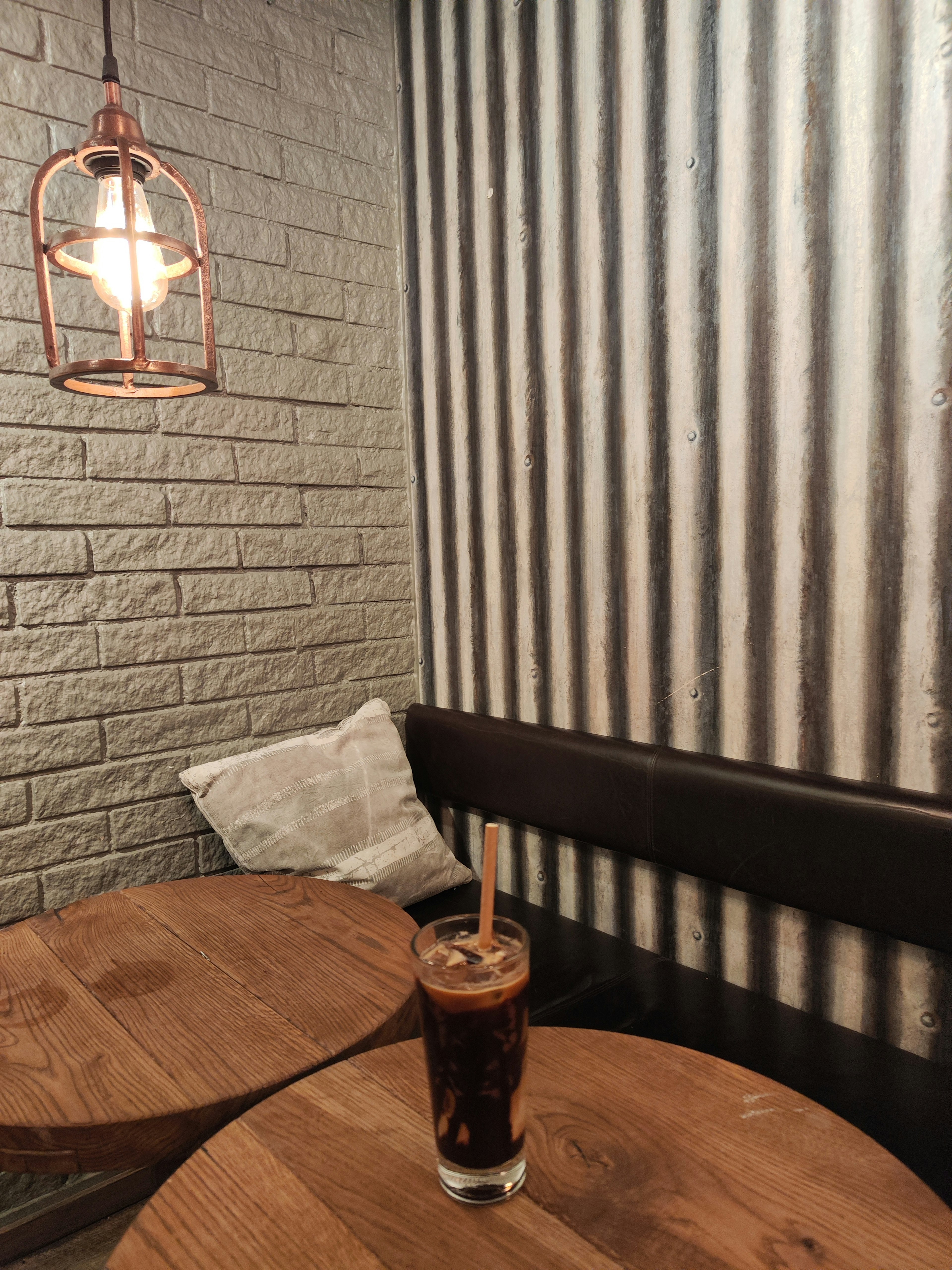 Interior of a cafe featuring a glass of coffee on a wooden table and a striped wall