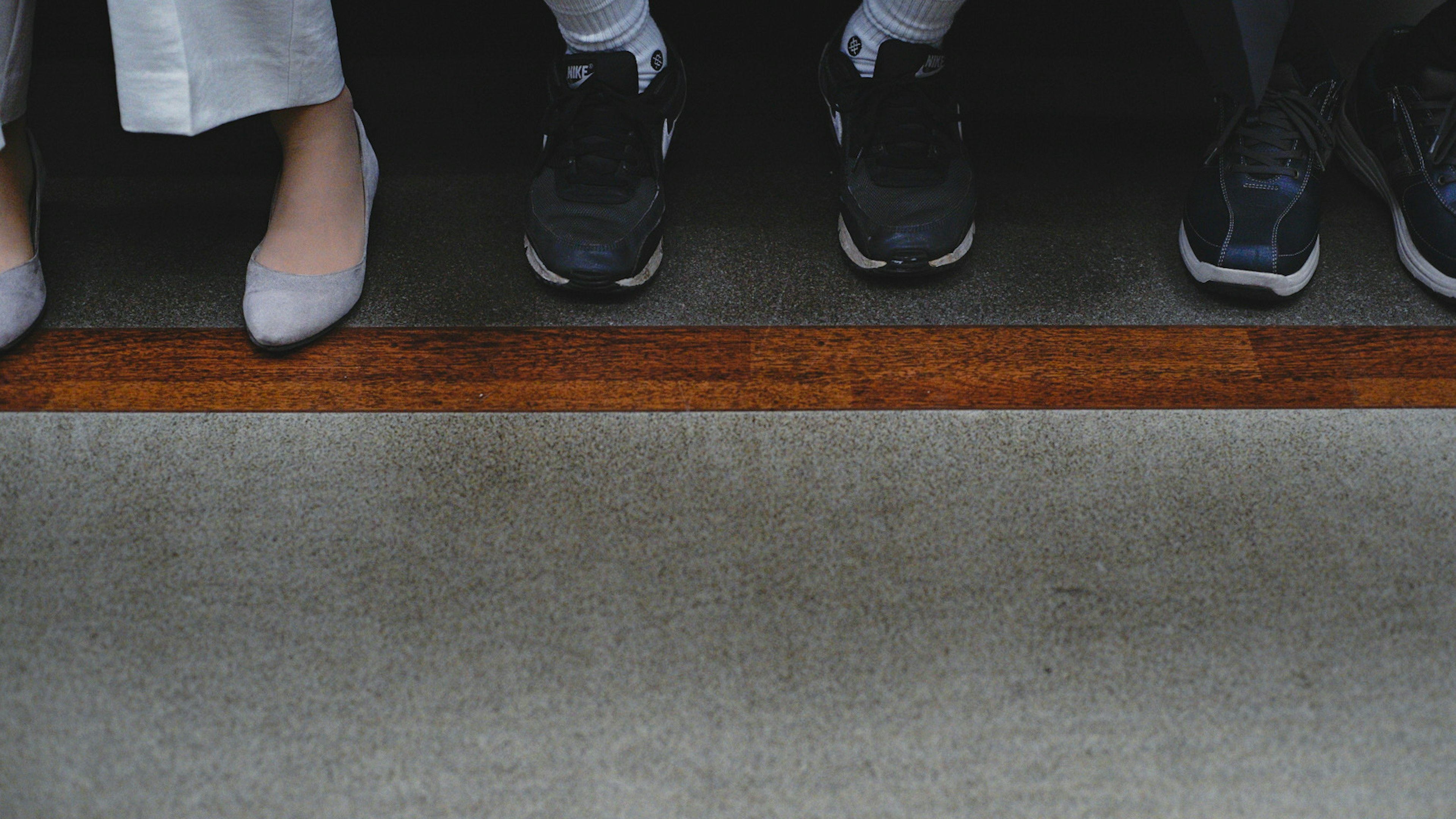 Scene featuring shoes and feet lined up with a distinctive wooden trim