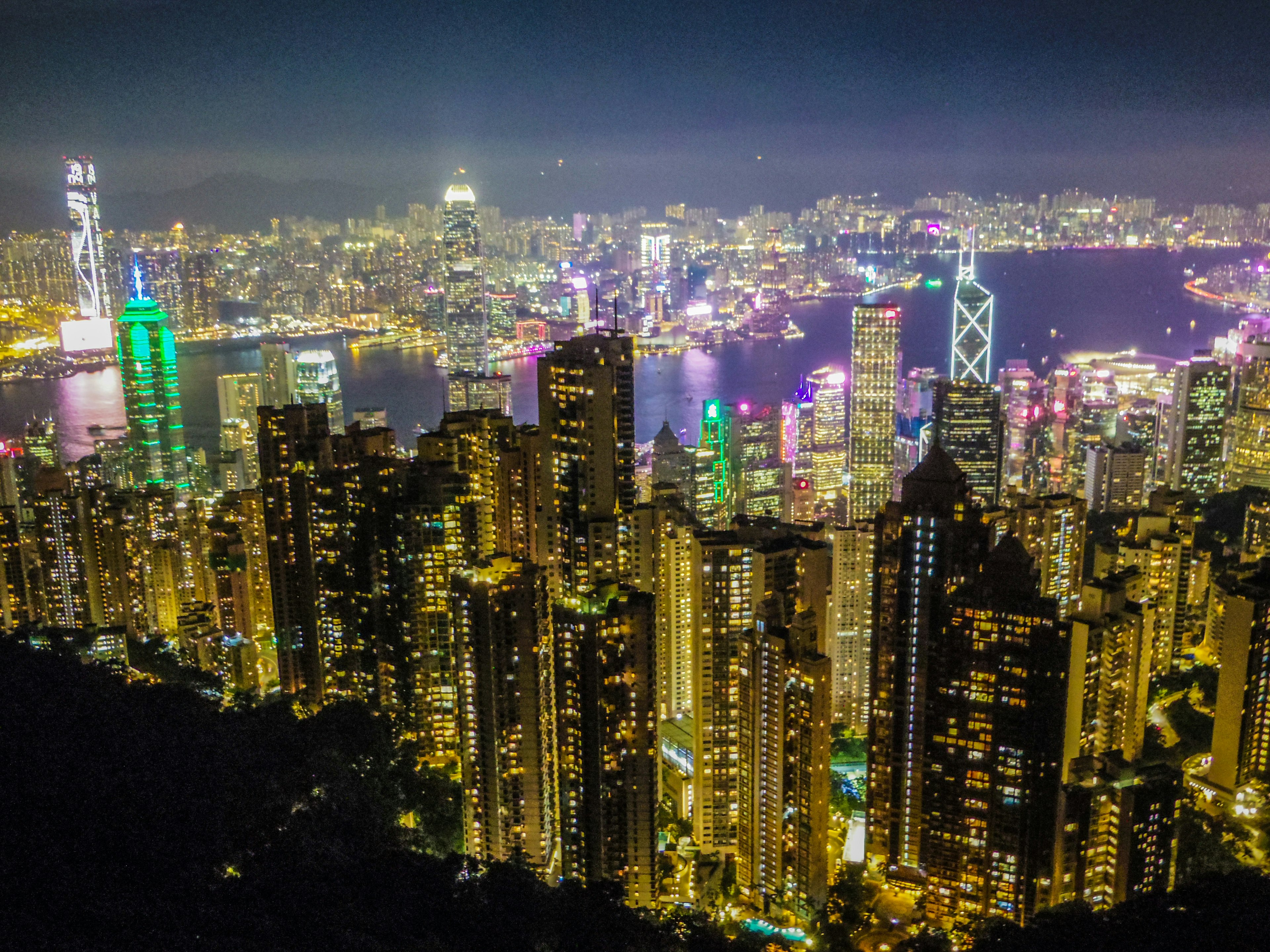 Una vista panorámica del horizonte de Hong Kong de noche con rascacielos iluminados y reflejos coloridos en el puerto