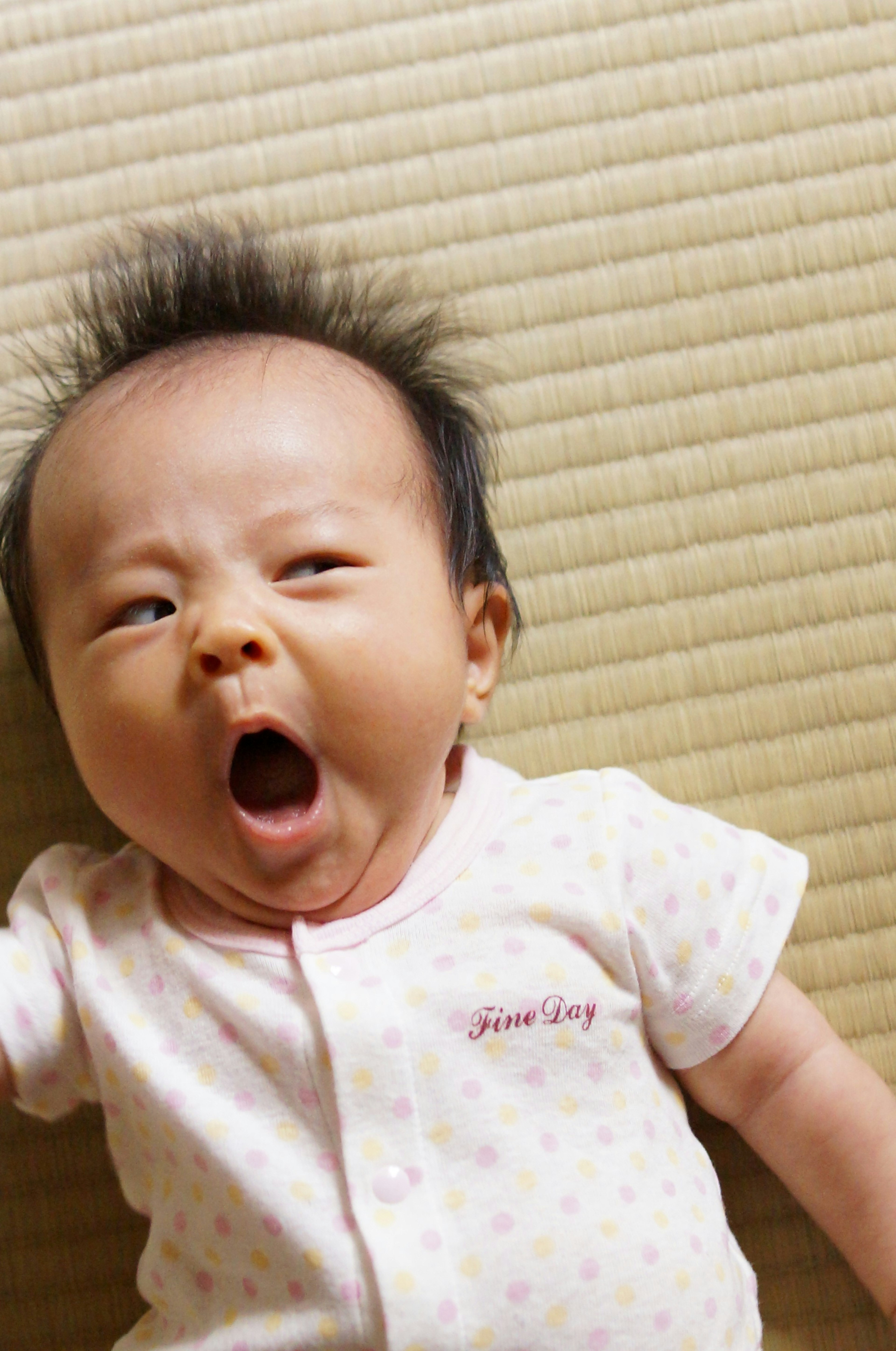 Baby yawning on tatami mat wearing a light-colored onesie