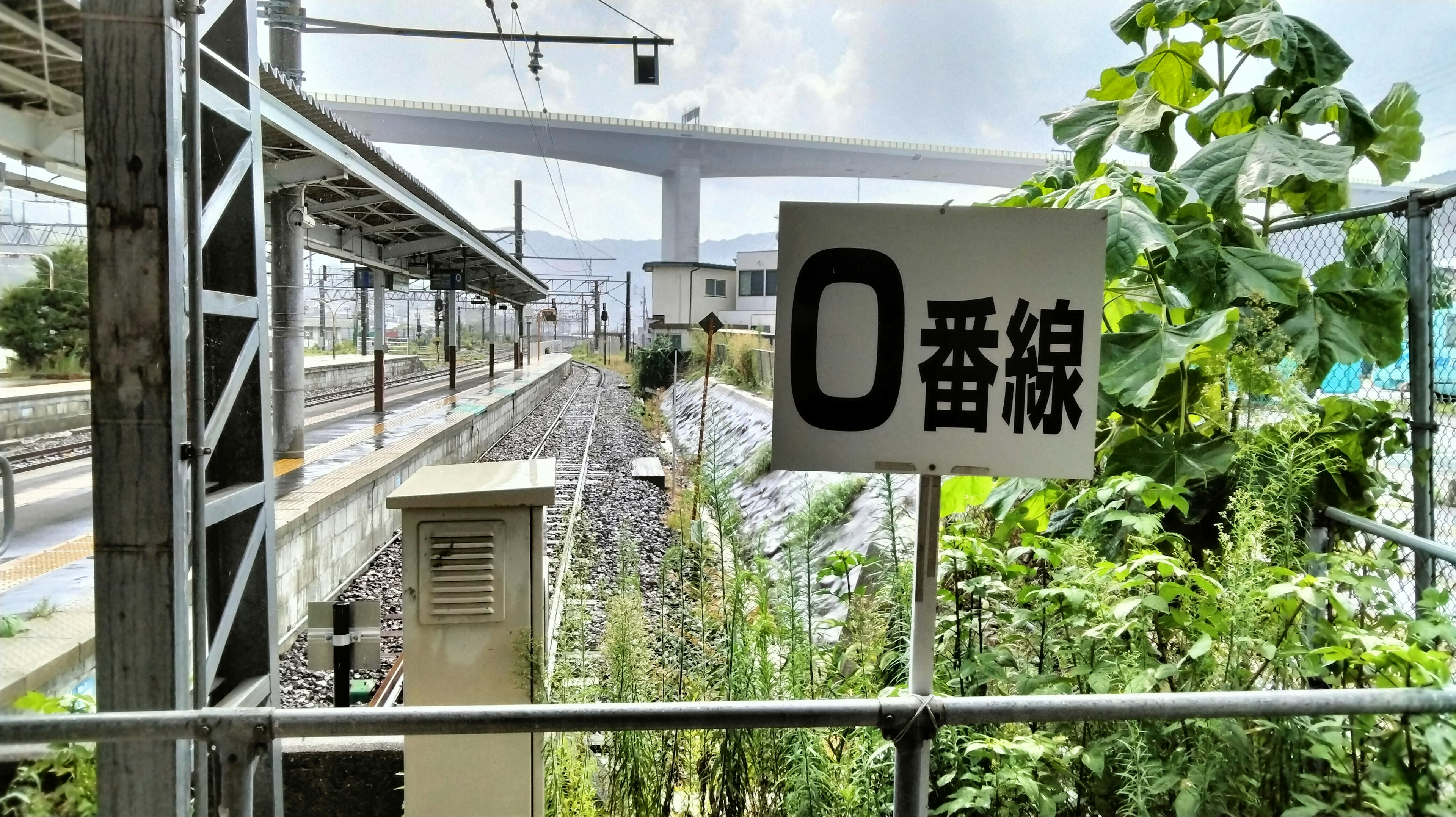 Platform sign for line 0 with surrounding greenery