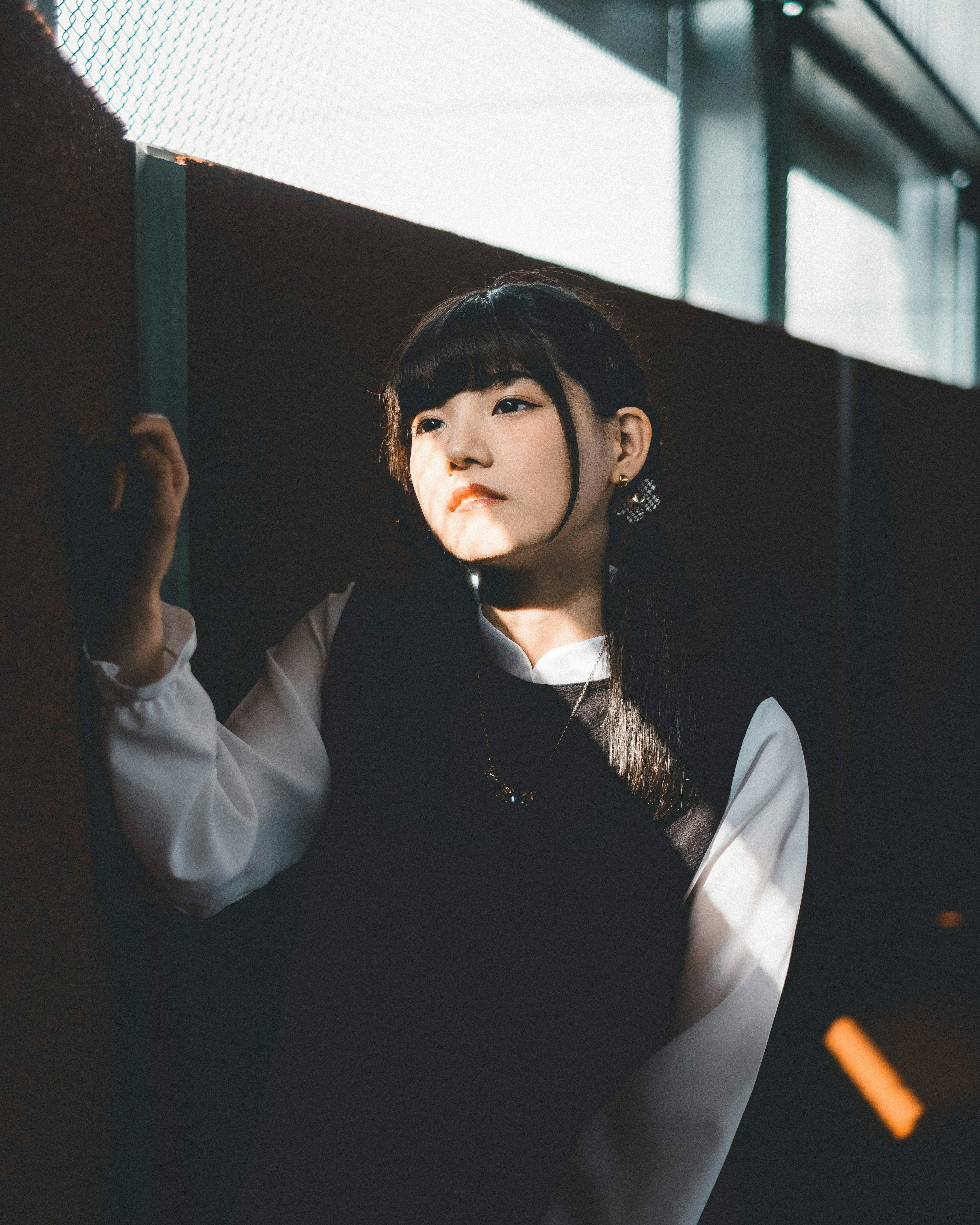 Young woman in black attire leaning against a wall in a beam of light