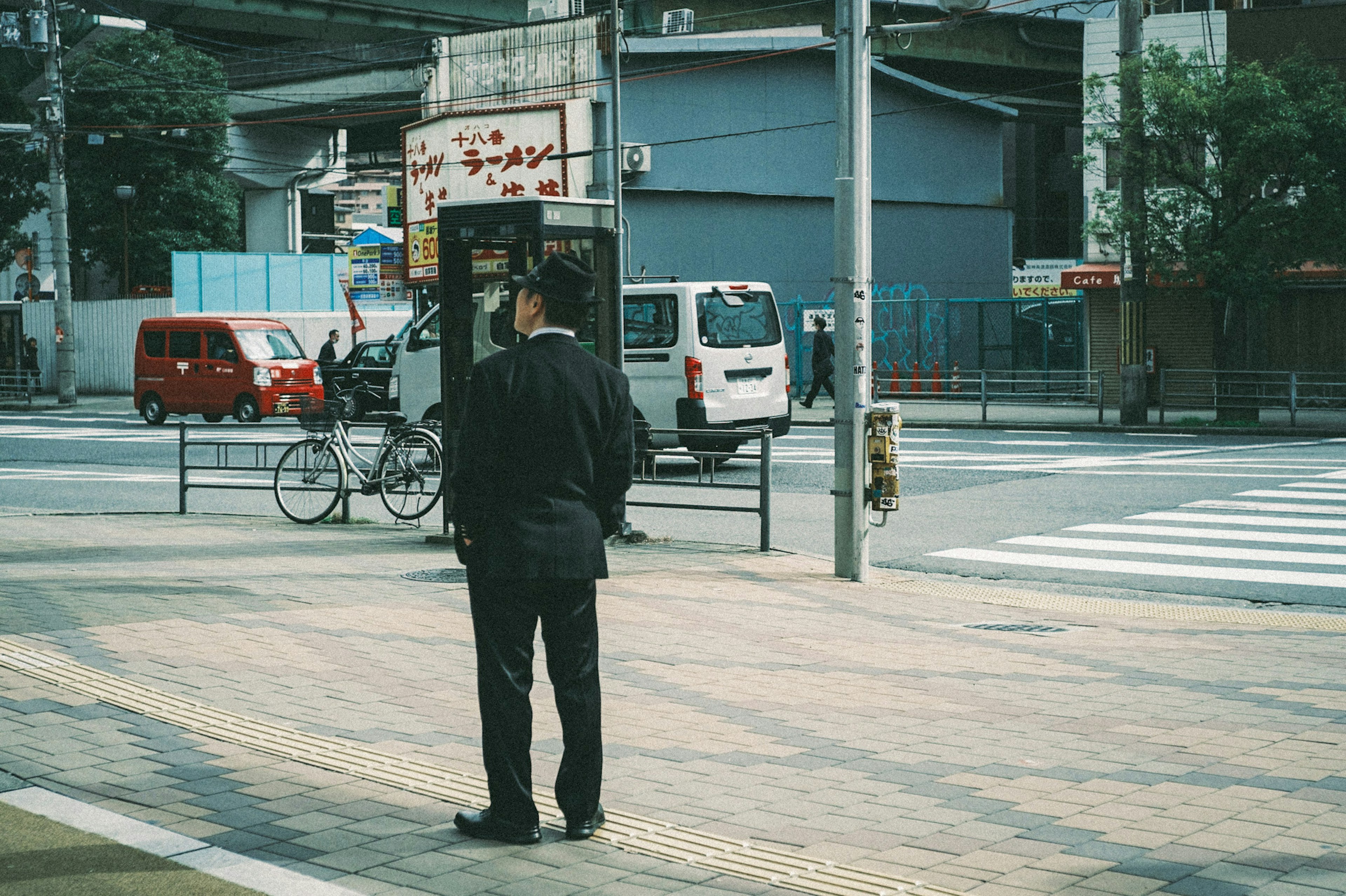 A man in a black suit standing at a crosswalk with an urban background