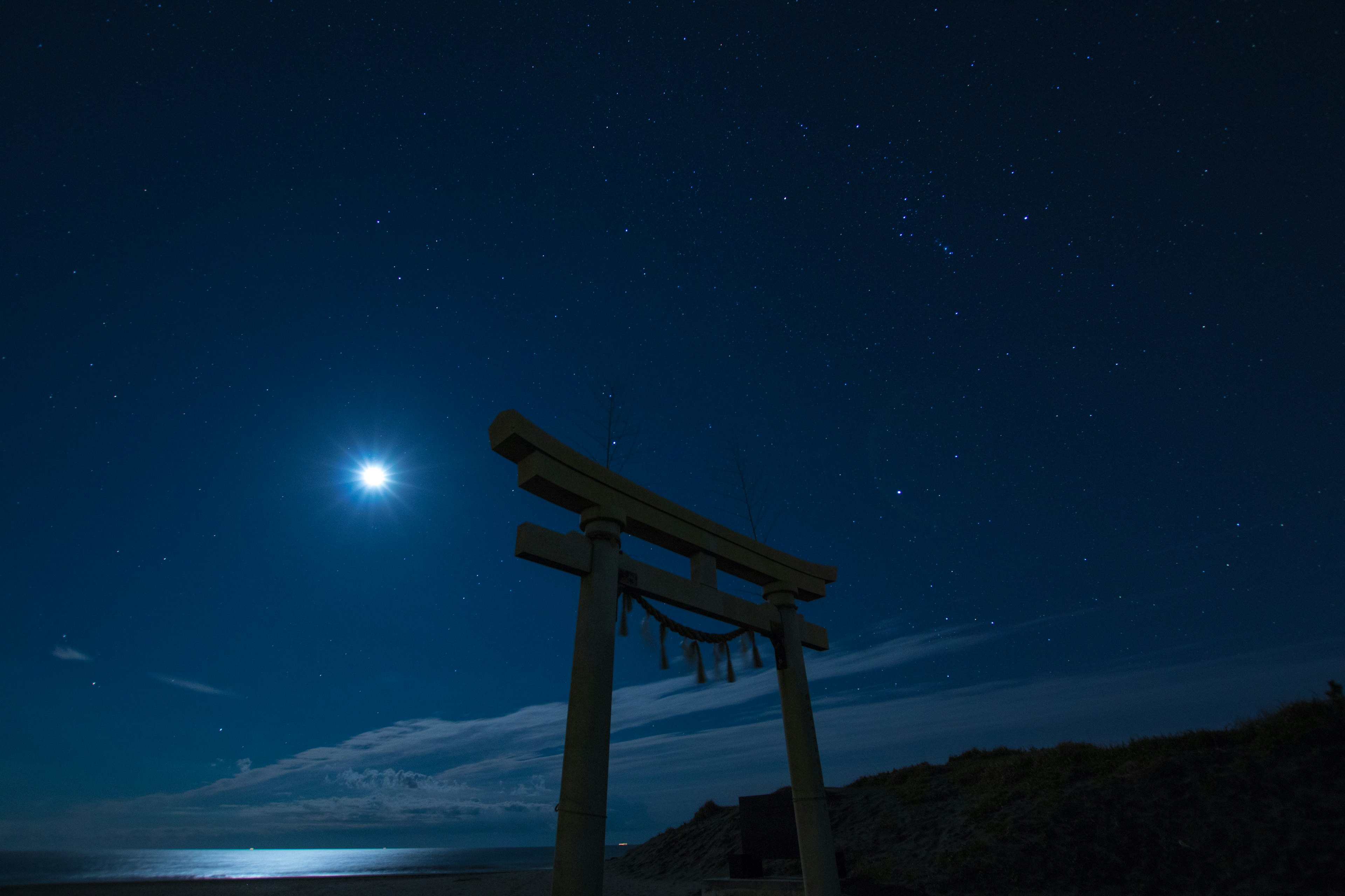 Gerbang torii yang diterangi cahaya bulan di bawah langit berbintang di atas lautan