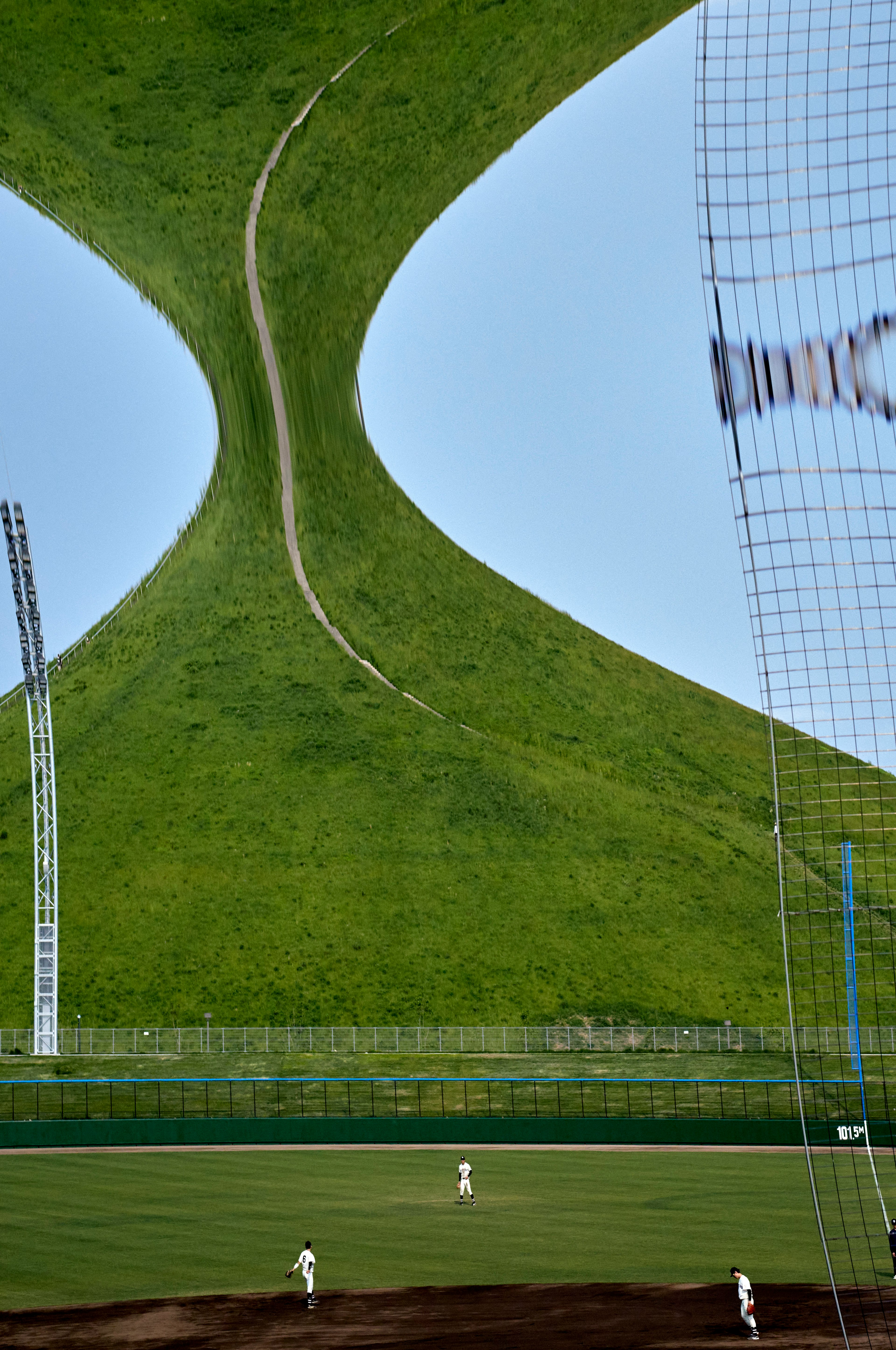 Terrain de baseball avec des collines vertes distinctives en arrière-plan joueurs visibles au loin